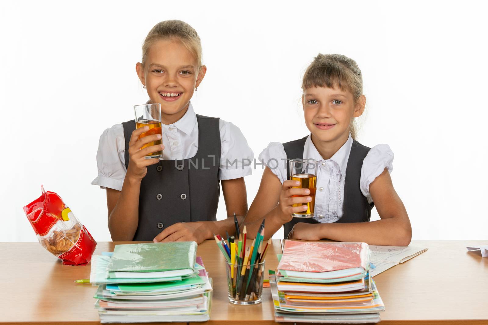 Two funny schoolgirls at a table drink juice, and look in the frame