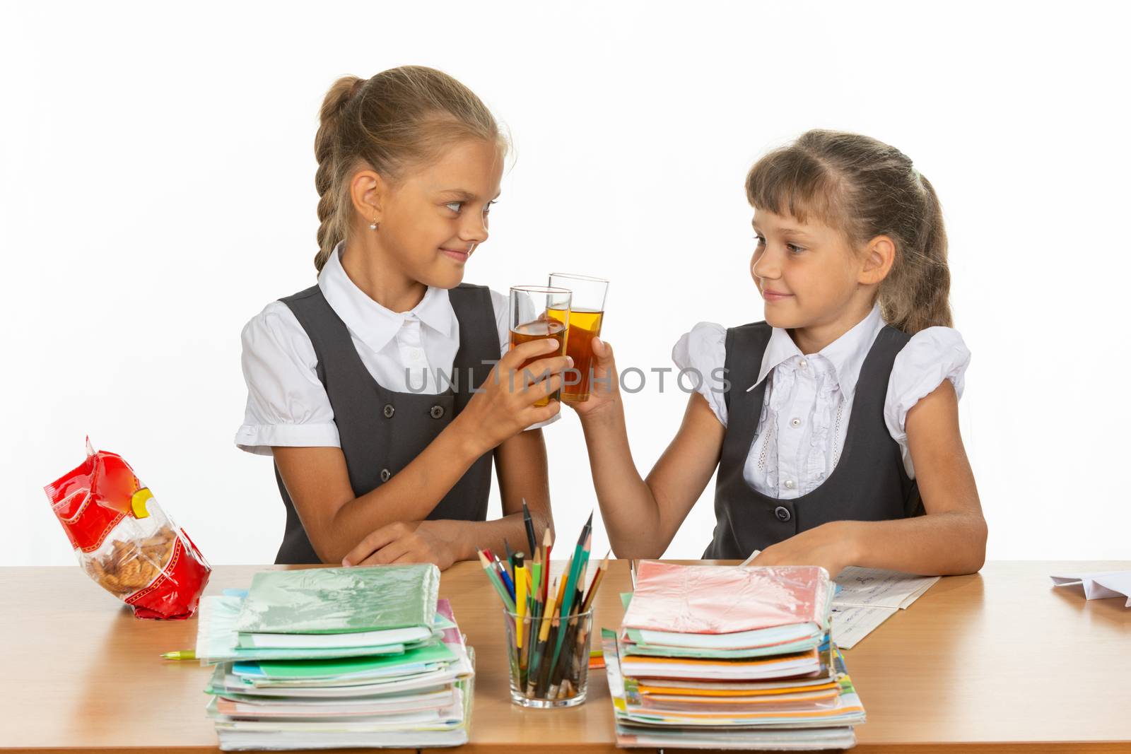 Two funny schoolgirls at a table drink juice, and banged glasses