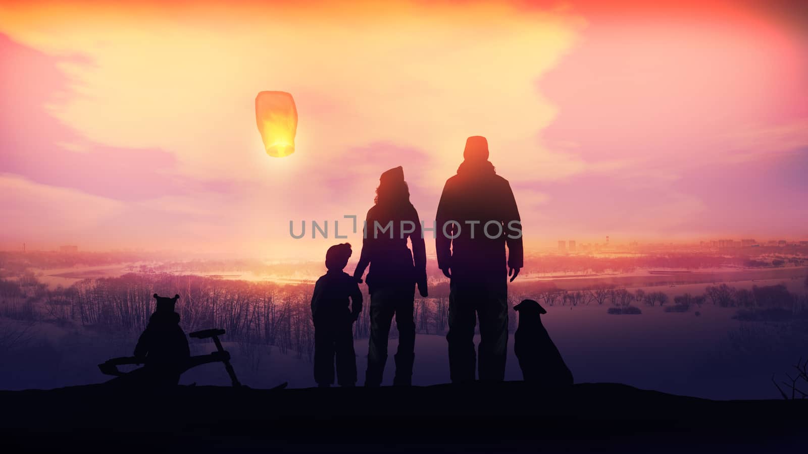 A family standing on a hill is launching a Chinese lantern on the background of a winter landscape at sunset.
