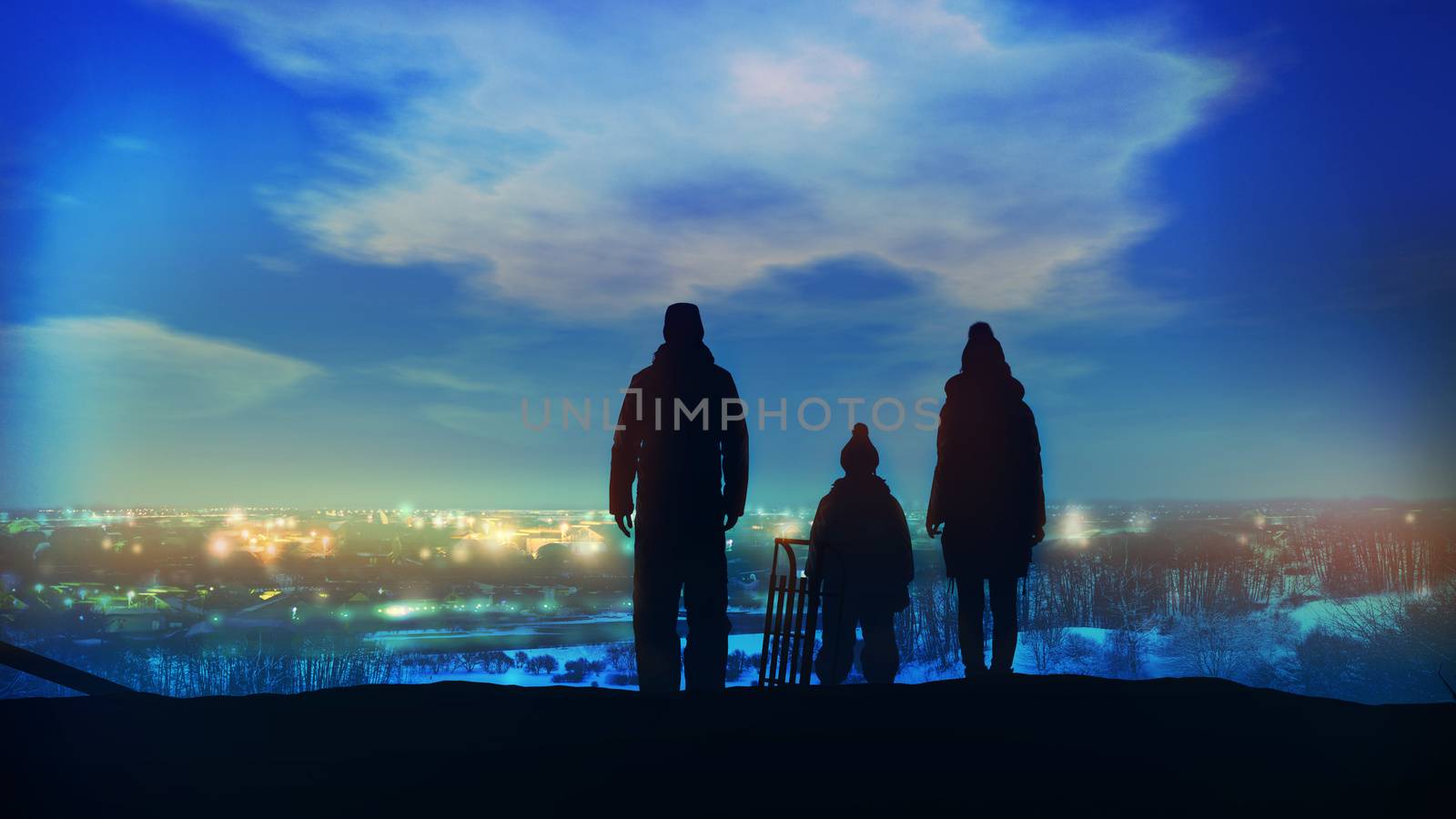 Family standing on a hill look at the evening lights of the Christmas city.