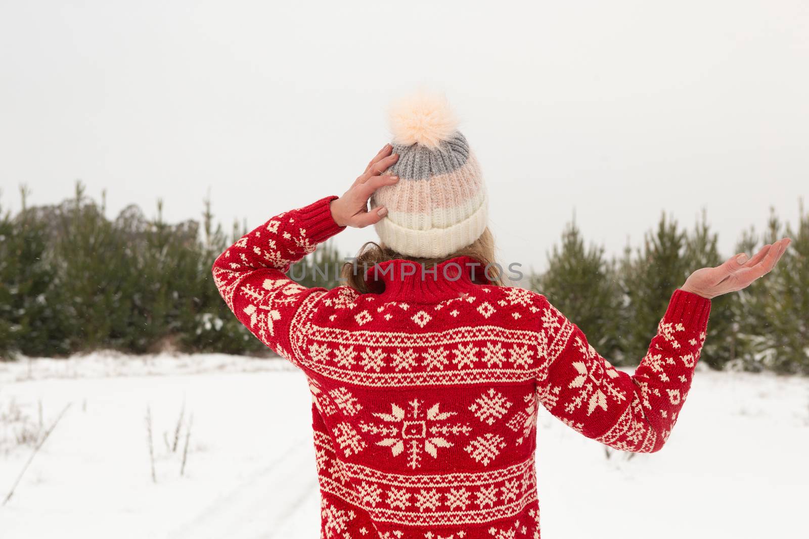 Woman wearing festive sweater and a cosy beanie standing in a winter landscape covered in snow with snow falling