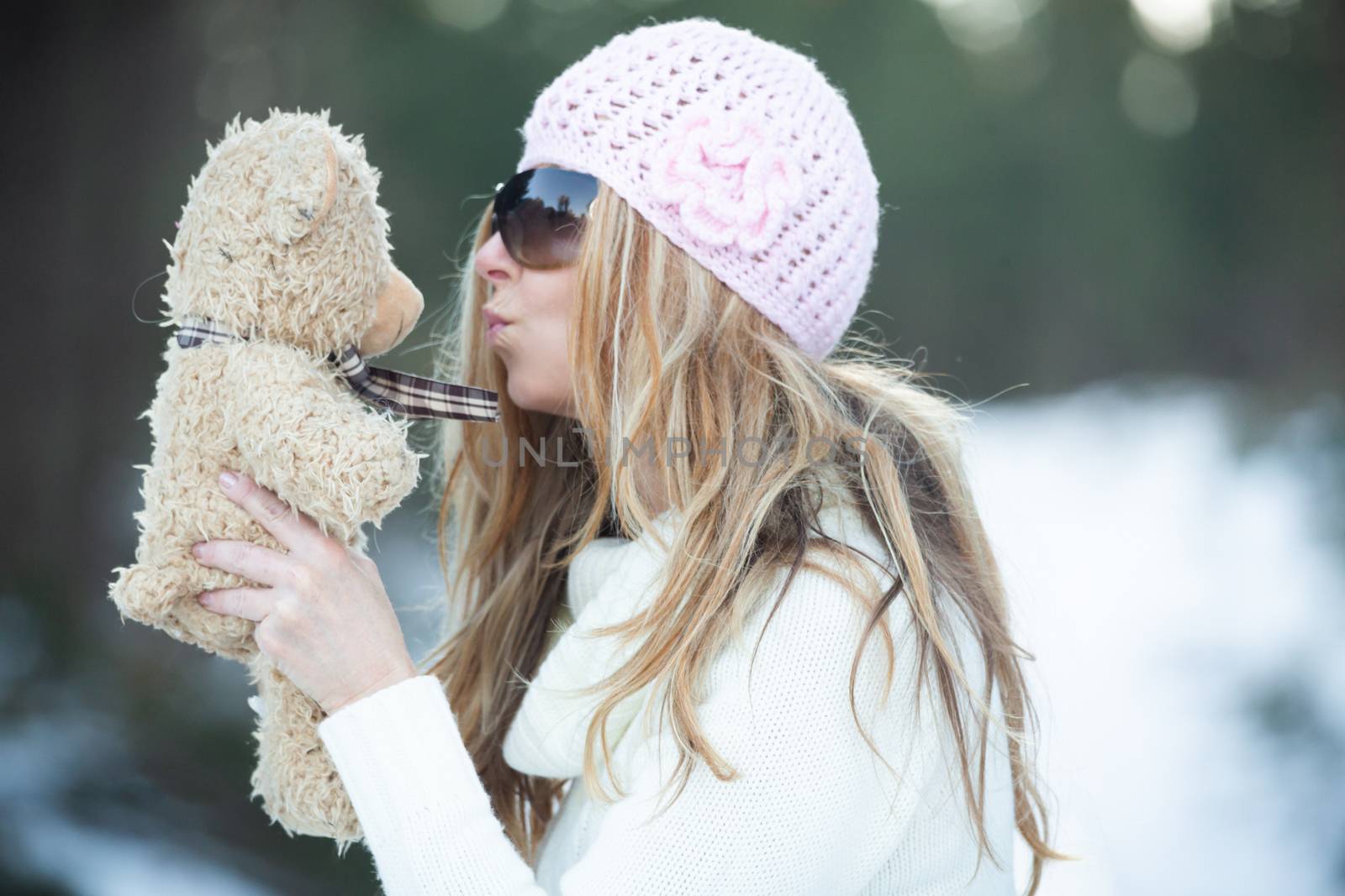 Woman blowing kisses to scruffy teddy bear in a snow covered winter landscape