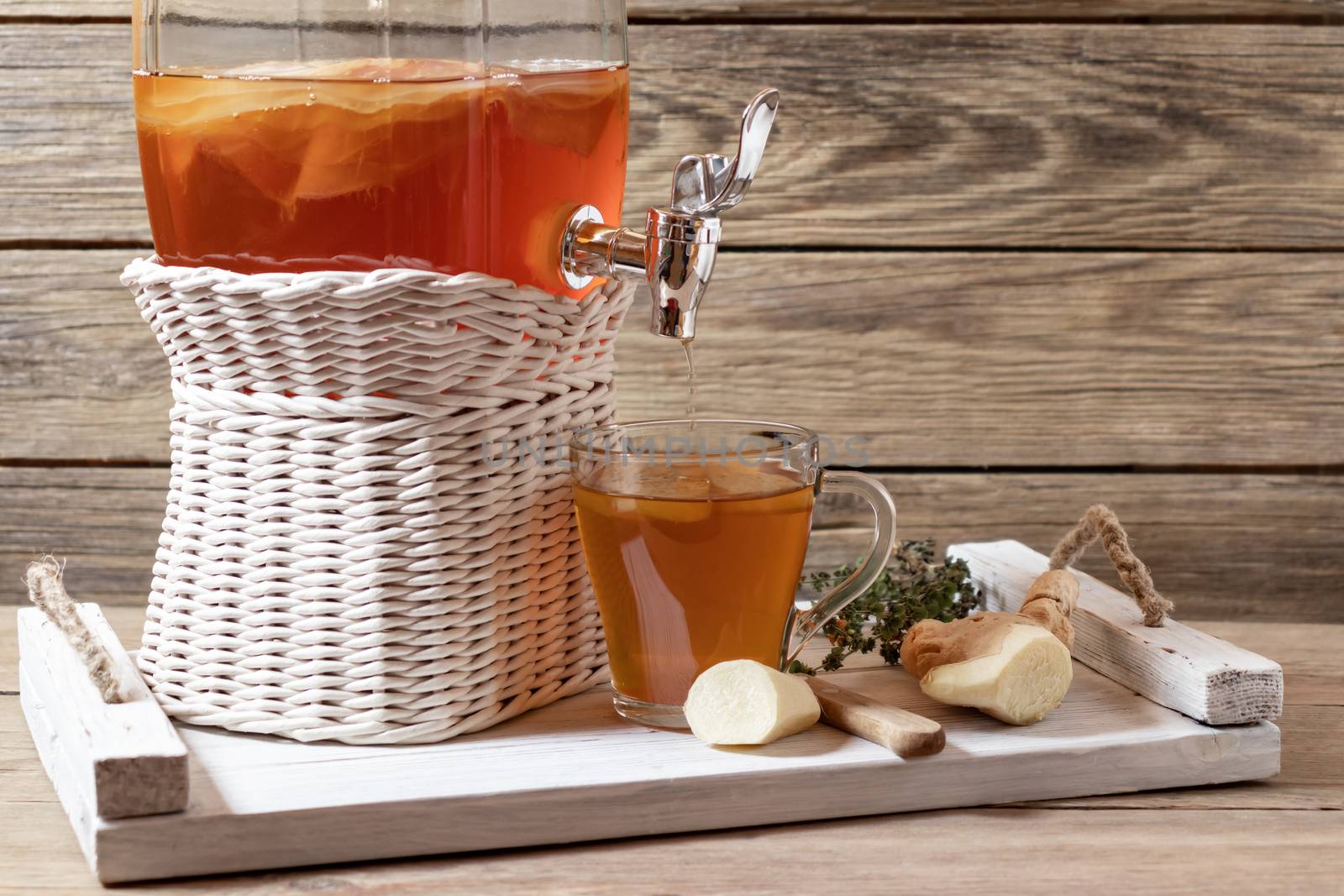 Fresh homemade kombucha fermented tea drink in a jar with faucet and in a cup on a white tray on a wooden background, copyspace by galsand