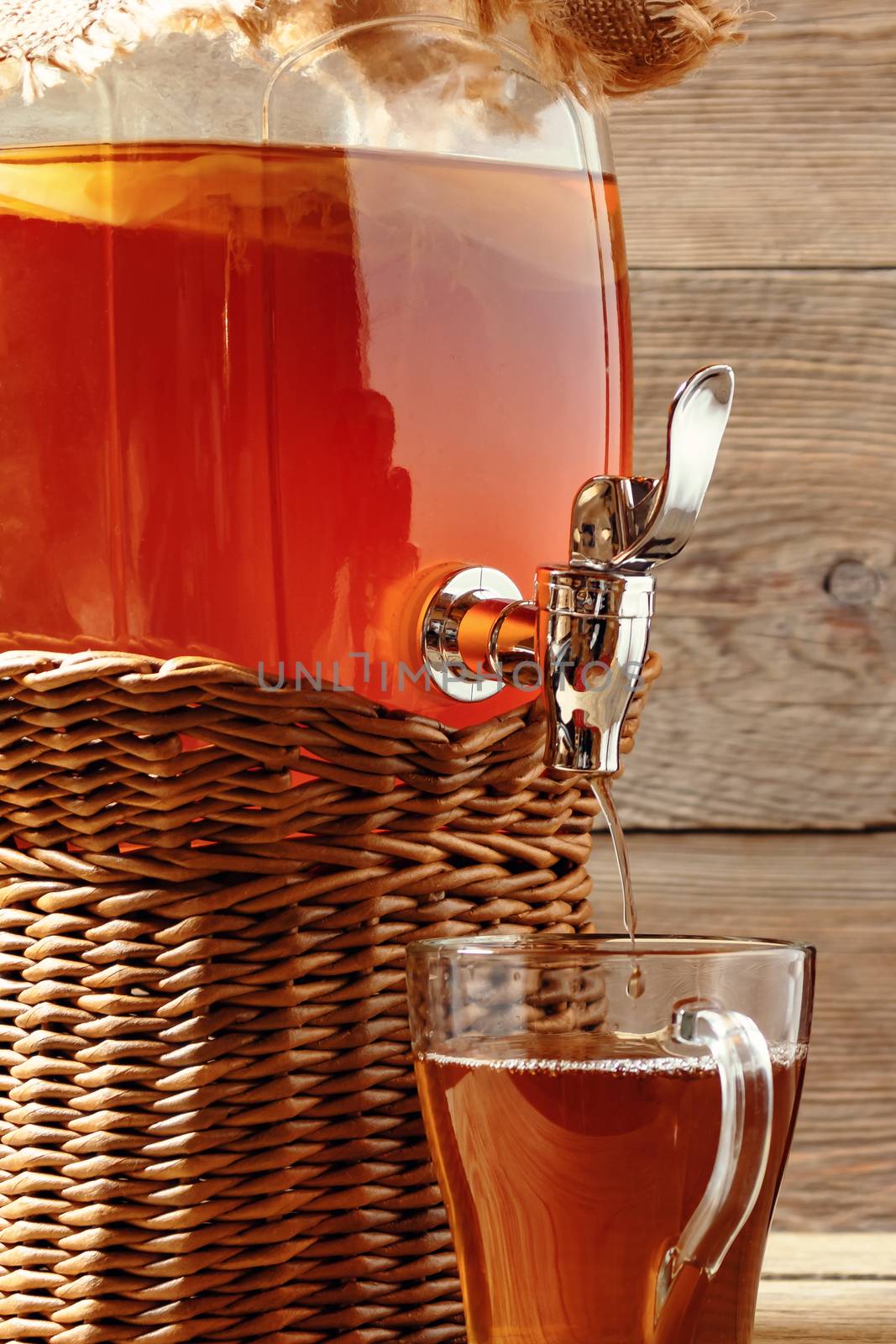 Fresh homemade Kombucha fermented tea drink in jar with faucet and in cup on wooden background, vertical image