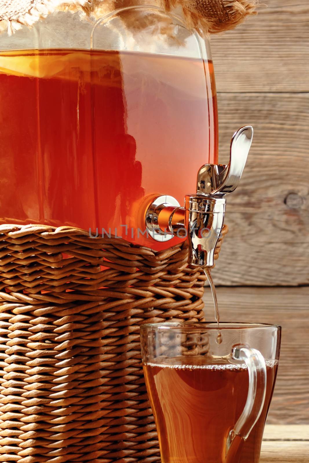 Fresh homemade Kombucha fermented tea drink in jar with faucet and in cup on wooden background. Vertical image by galsand