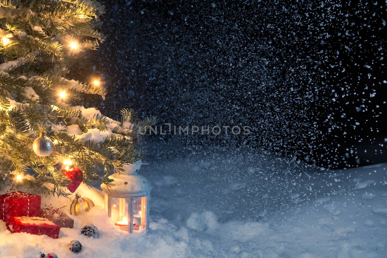 Christmas composition - gifts and a lantern in the snow under a Christmas tree decorated with lights and Christmas-tree decorations, copy space, place for text.