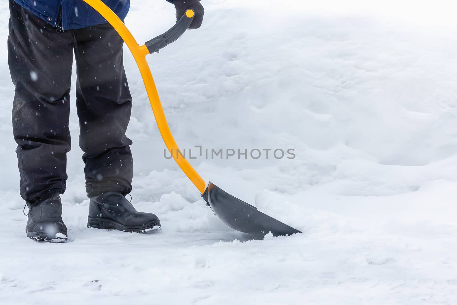 A man cleans snow in the yard with a shovel after a heavy snowfall.