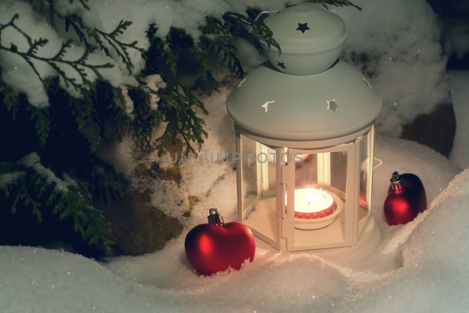 Lantern with a burning candle under a snow-covered Christmas tree in the courtyard of the house in the snowdrifts.