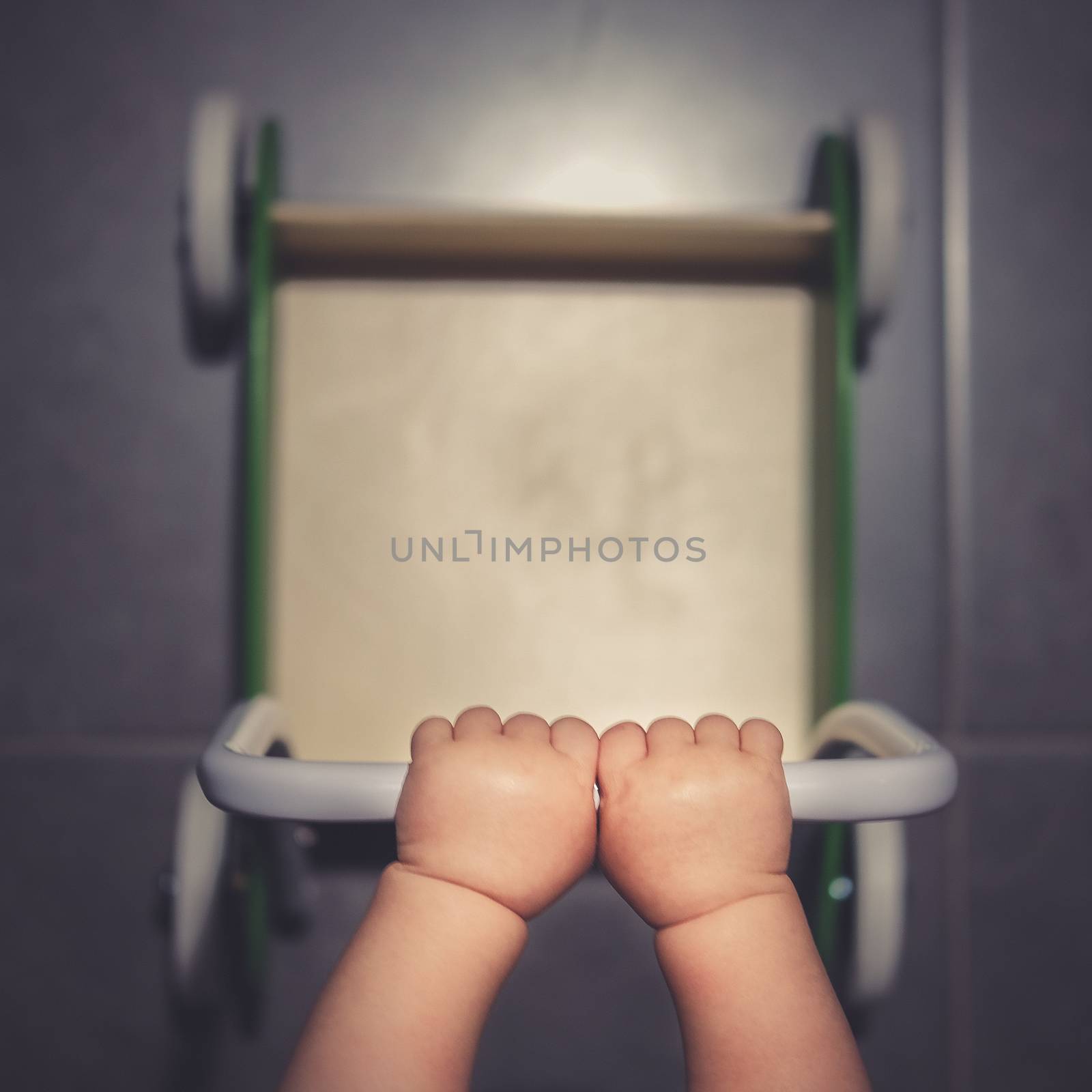 Little babys chubby hands pushing a green wooden walker on the kitchen tiles