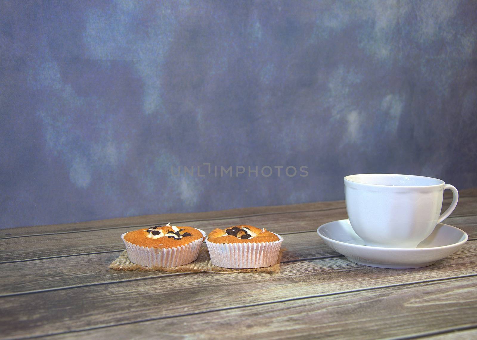 A cup of tea on a saucer and two cupcakes on a textile napkin. by alexey_zheltukhin