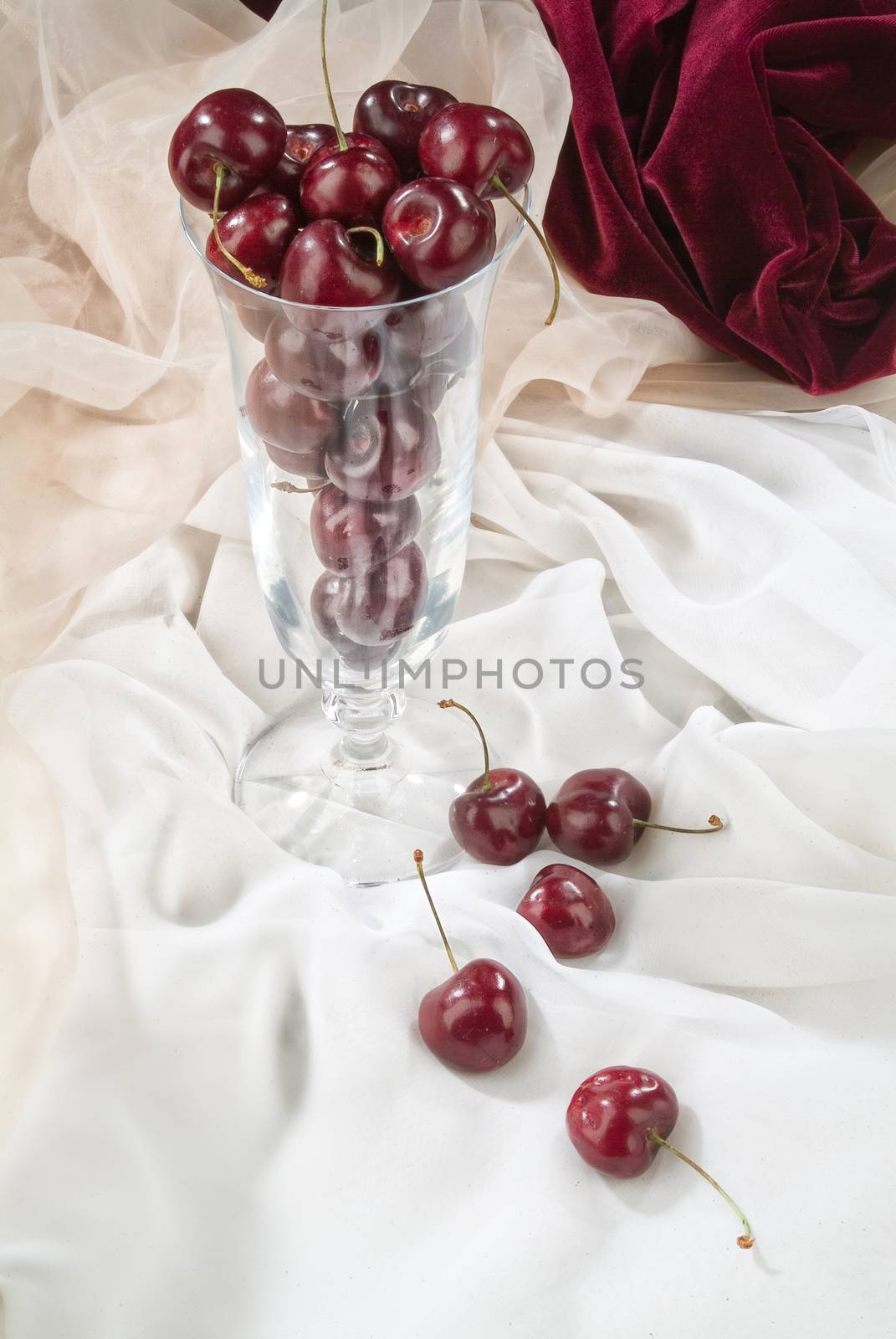 Cherries and glass on a studio fabric background