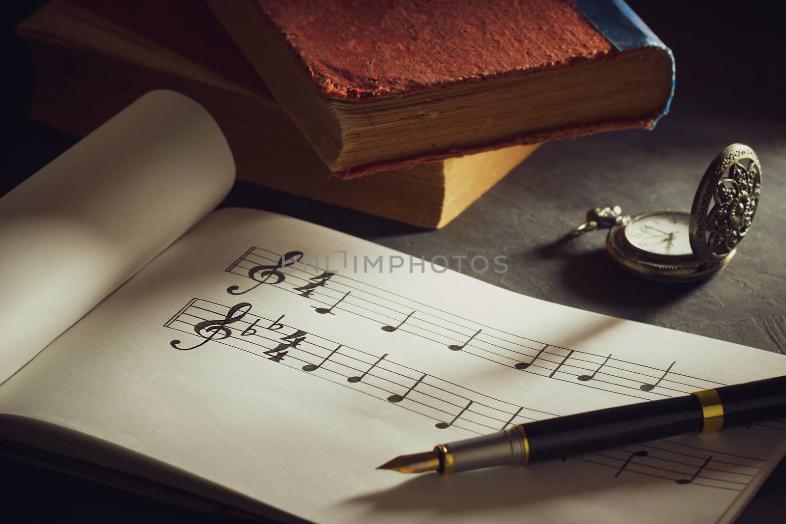 Music notes and old book with pocket watch on wooden table background in morning light. Writing chords by vintage pen. Closeup and copy space for text. Concept of Music lovers.