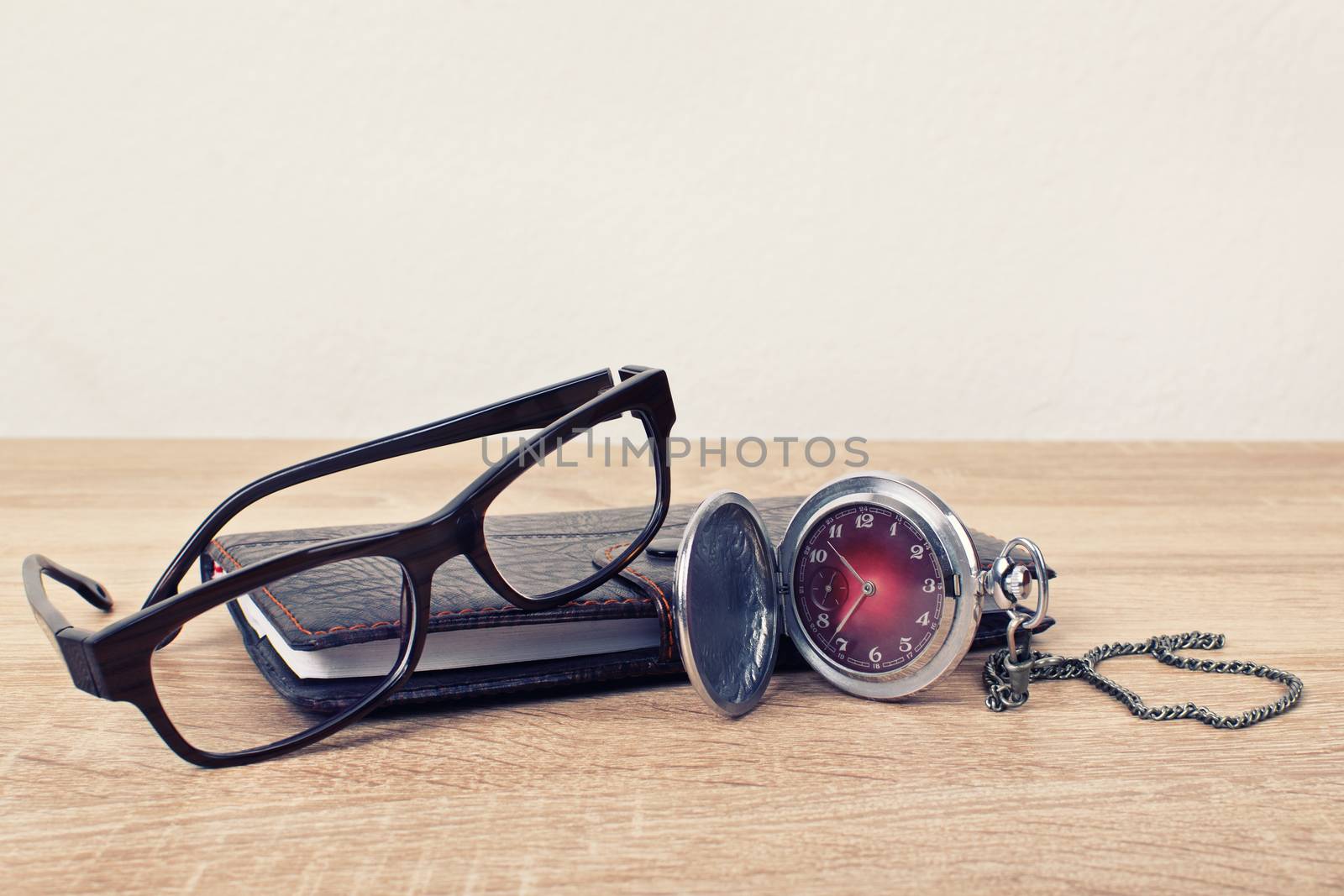 Pocket watch, glasses and a planner on a table by Mendelex