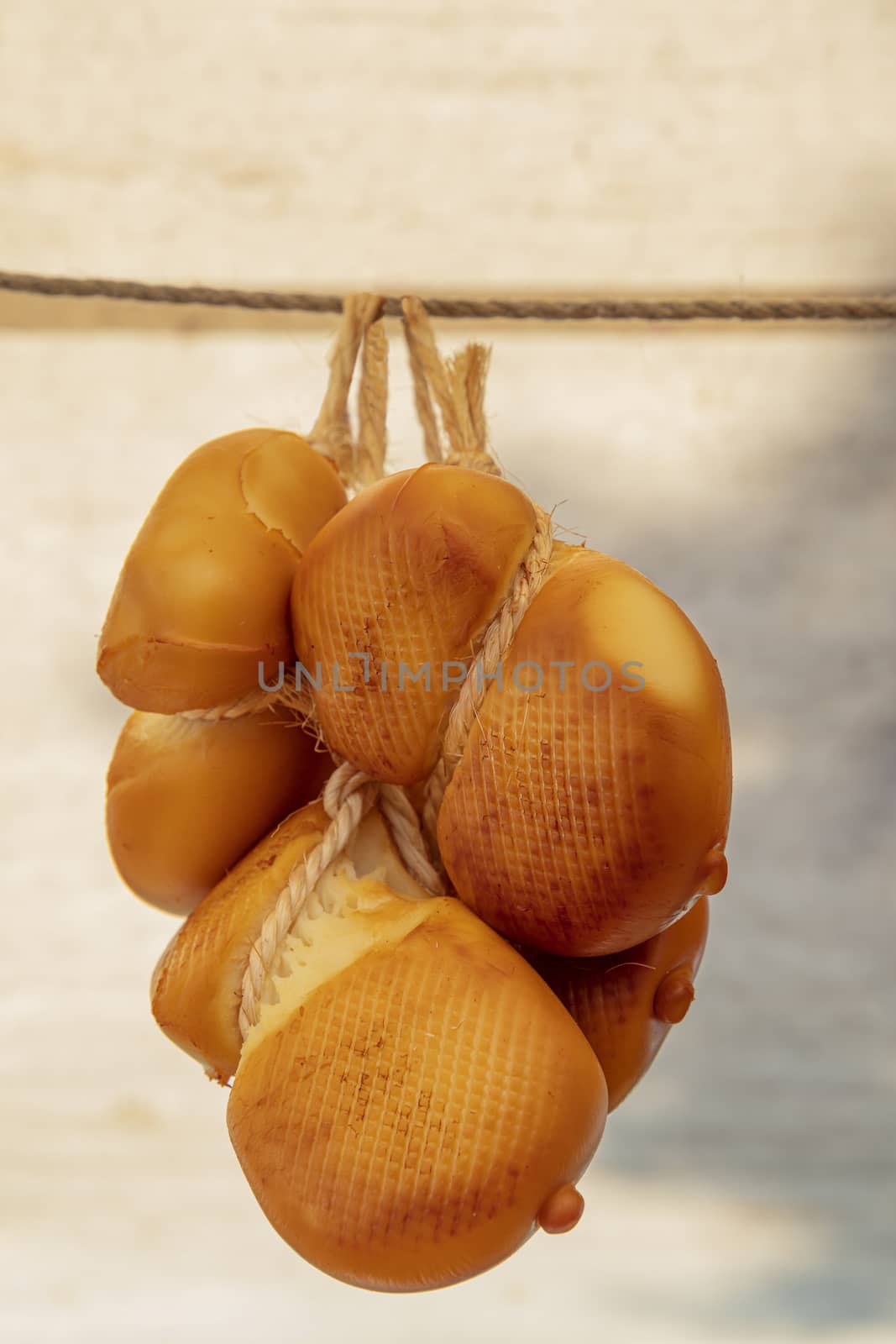 Close up group of several traditional smoked artisanal Italian Scamorza affumicata cheese heads hanging in retail, low angle side view
