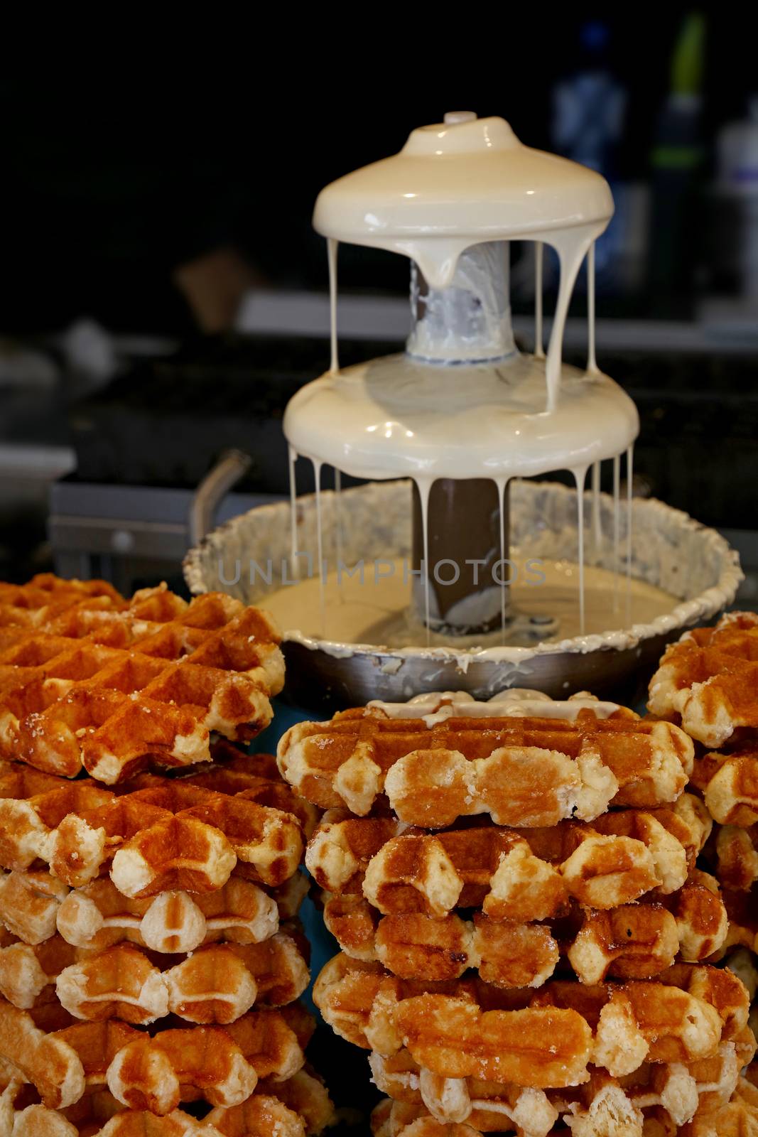 Close up of Belgian liquid white chocolate fountain for sweet fondue dip desserts and traditional wafers, low angle view