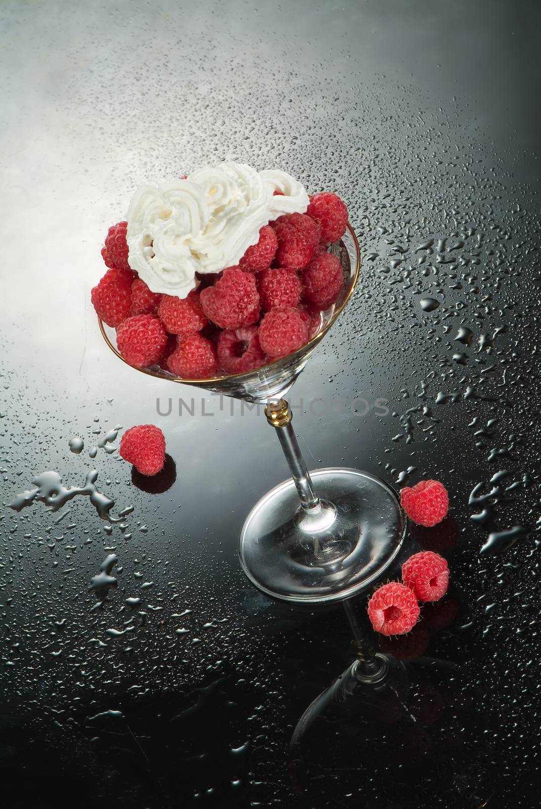 Glass with raspberries and cream on a glass background