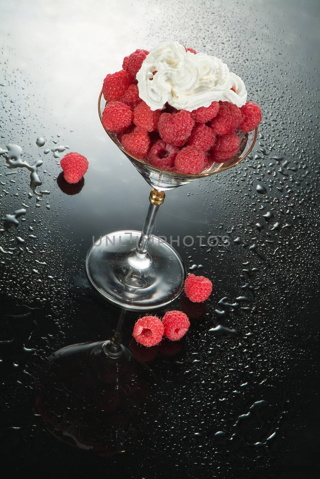Glass with raspberries and cream on a glass background