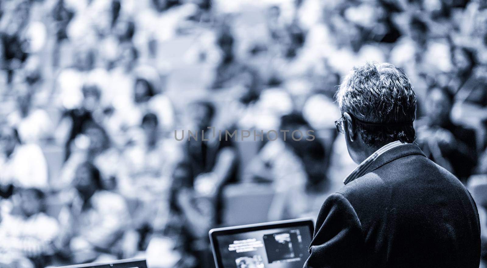 Speaker giving a talk on corporate business conference. Unrecognizable people in audience at conference hall. Business and Entrepreneurship event. Black and white, blue toned image.