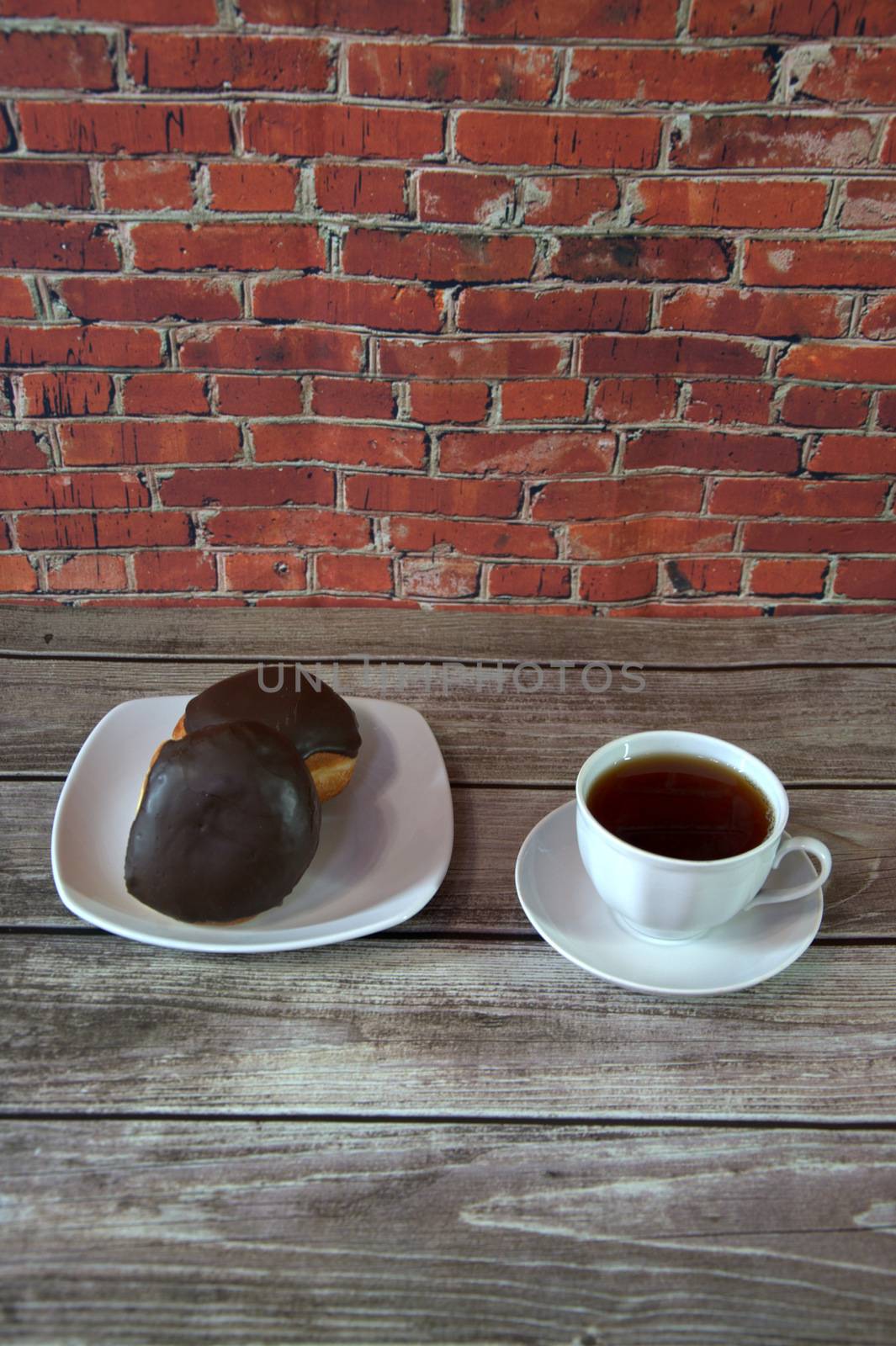 A cup of coffee and two donuts in a chocolate eye on a white ceramic plate. Close-up.