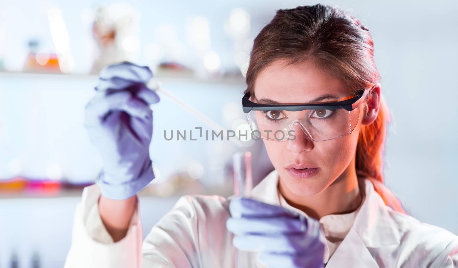 Life scientists researching in laboratory. Focused female life science professional pipetting solution into the glass cuvette. Lens focus on researcher's eyes. Healthcare and biotechnology concept.