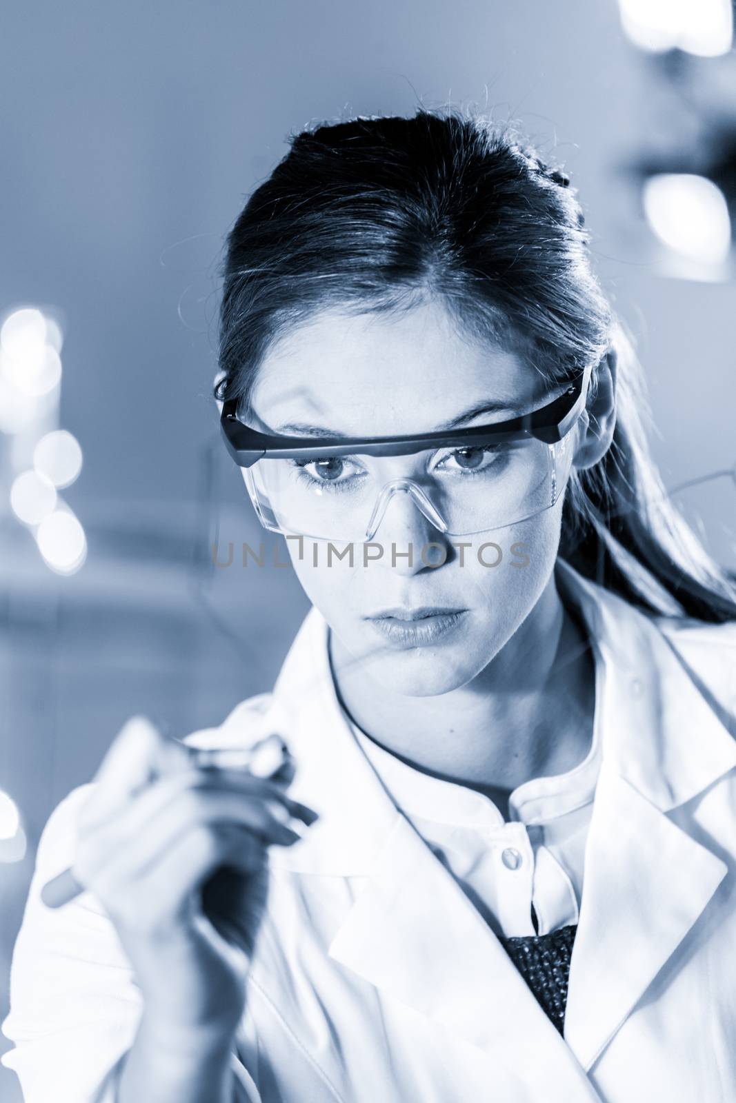 Portrait of a confident female health care expert in life science laboratory writing structural chemical formula on a glass board. Healthcare and modern life science concept. Blue toned image.