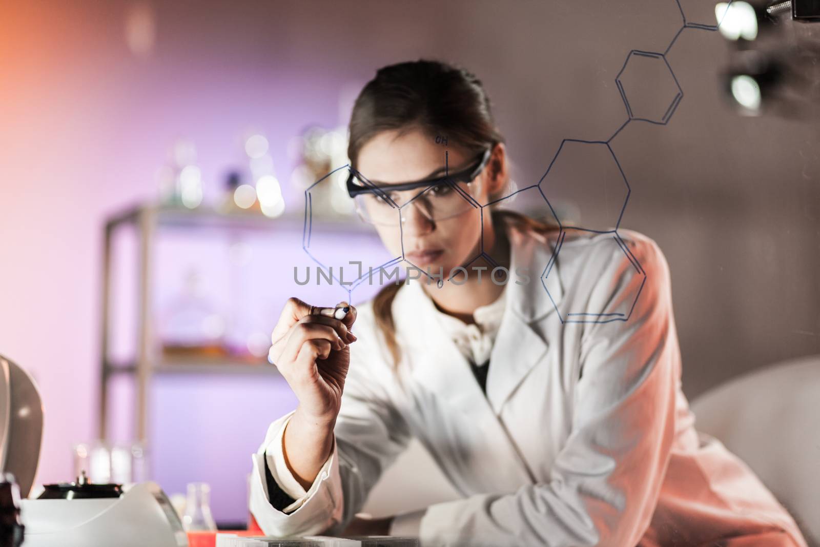 Portrait of a confident female researcher in life science laboratory writing structural chemical formula on a glass board. by kasto