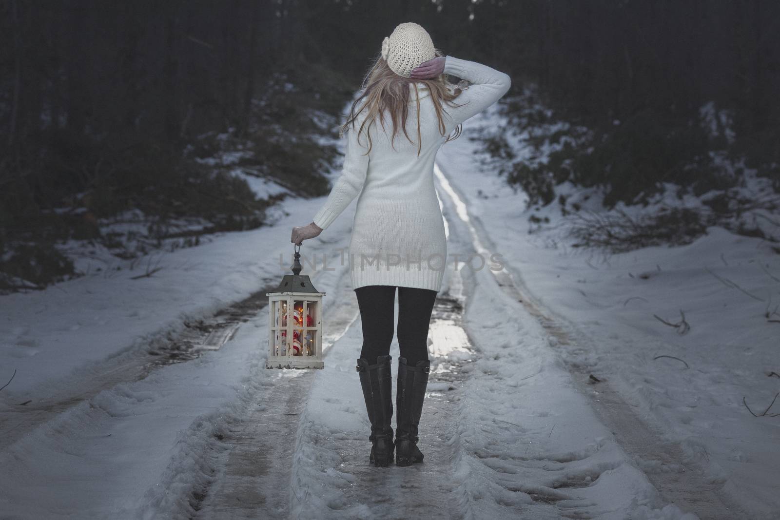 Woman walking along an icy road through forest in winter with lantern