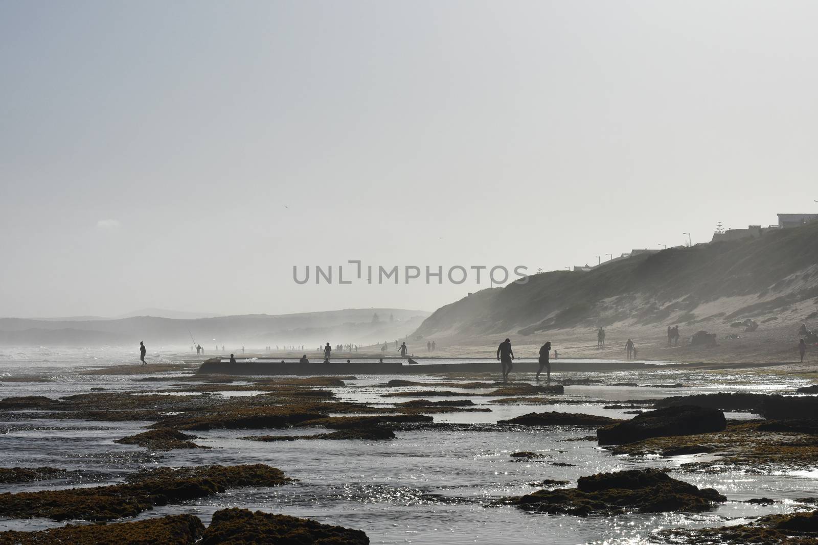 Mossy rock pools on the African south coast with beach goers, Mossel Bay, South Africa