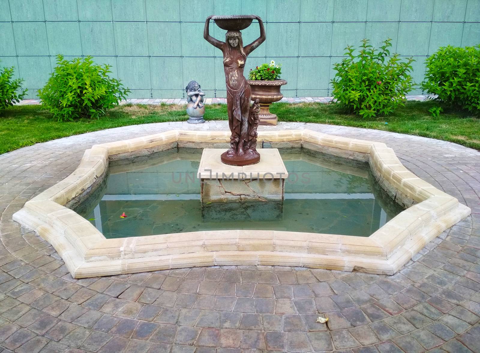 Statue of a girl in Greek clothes with a bowl on her head in the center of the fountain.