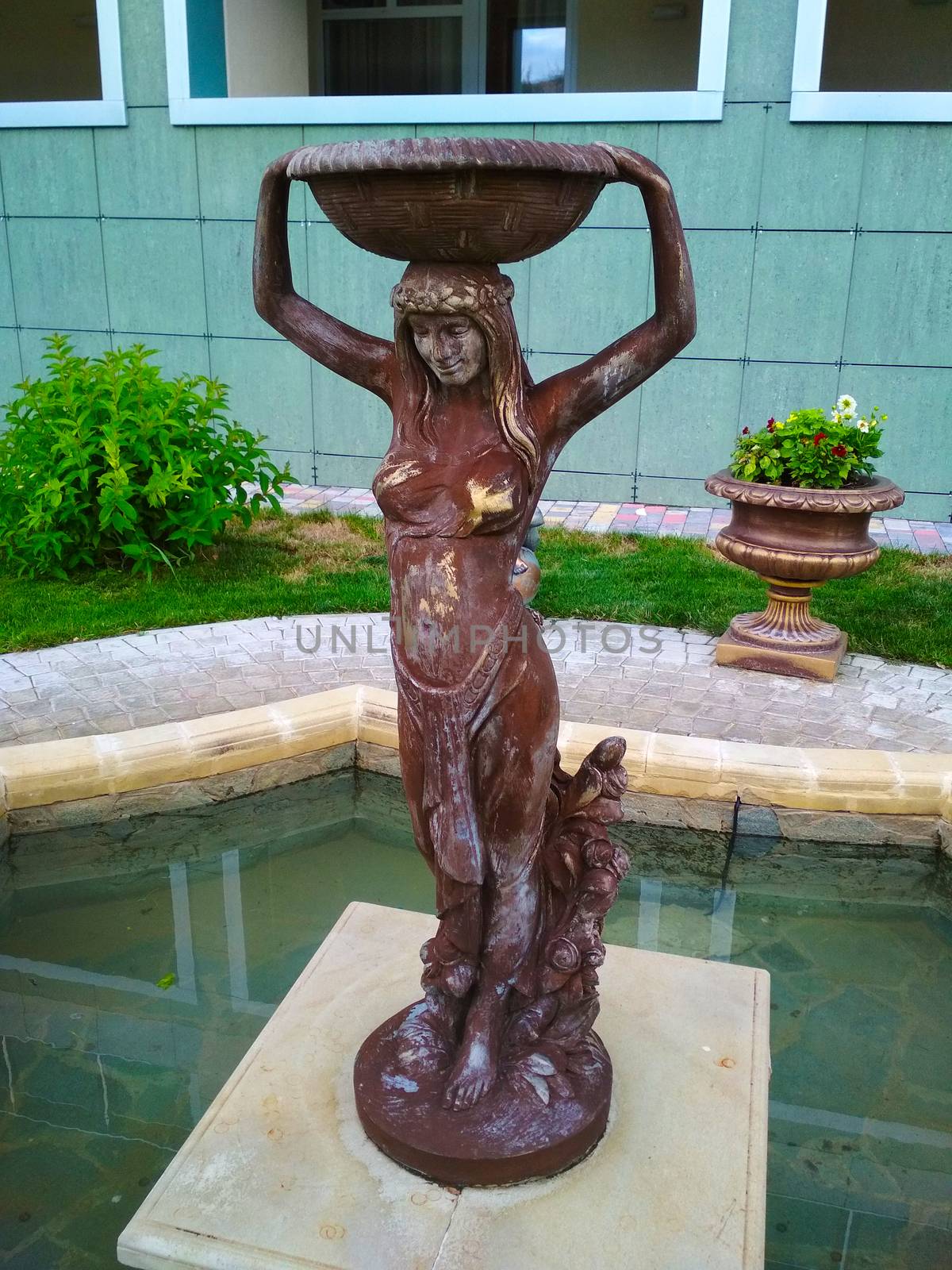 A statue of a girl in a brick-colored tunic with a tray and a wreath on her head.