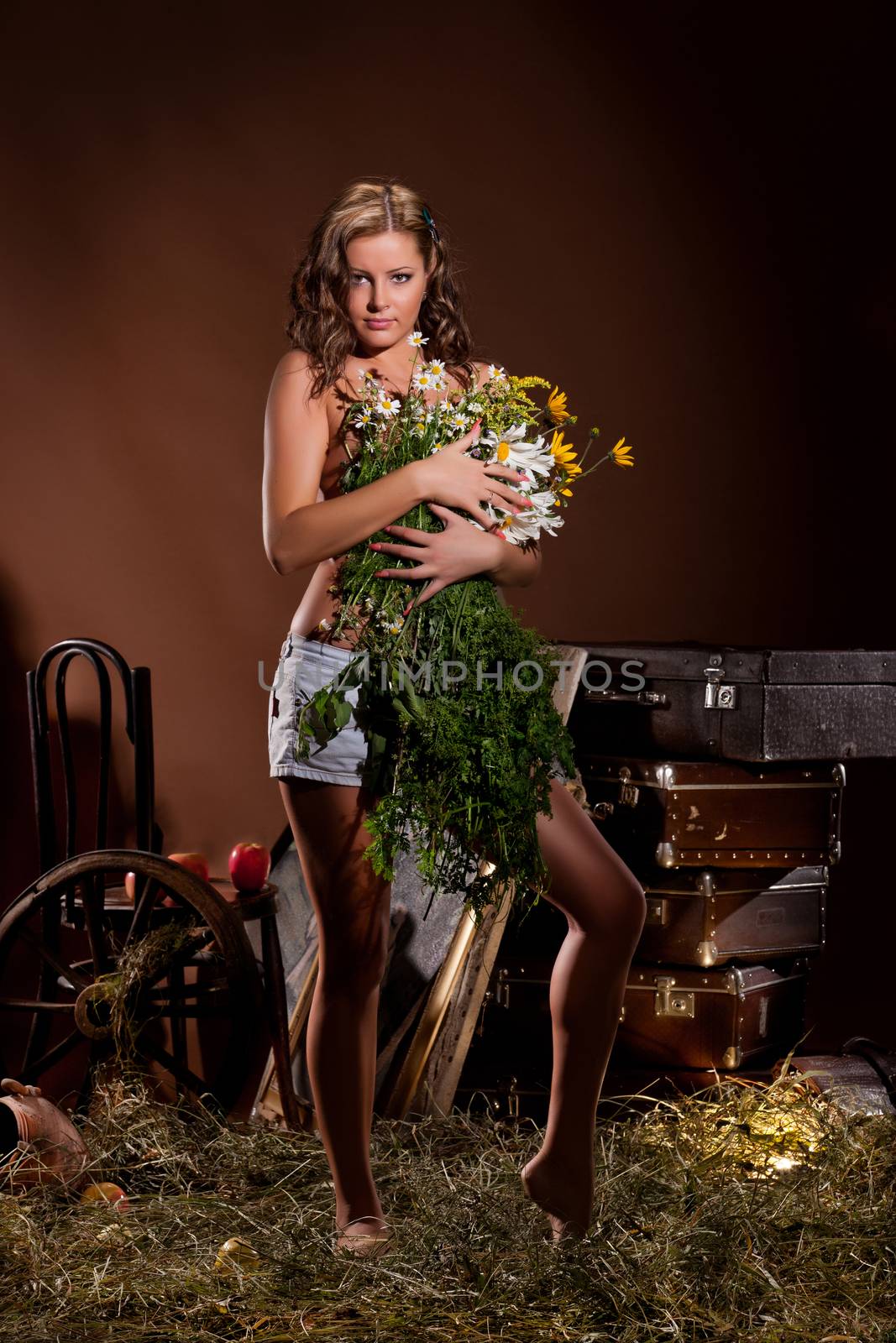 Young beautiful topless woman with flowers standing on a hay