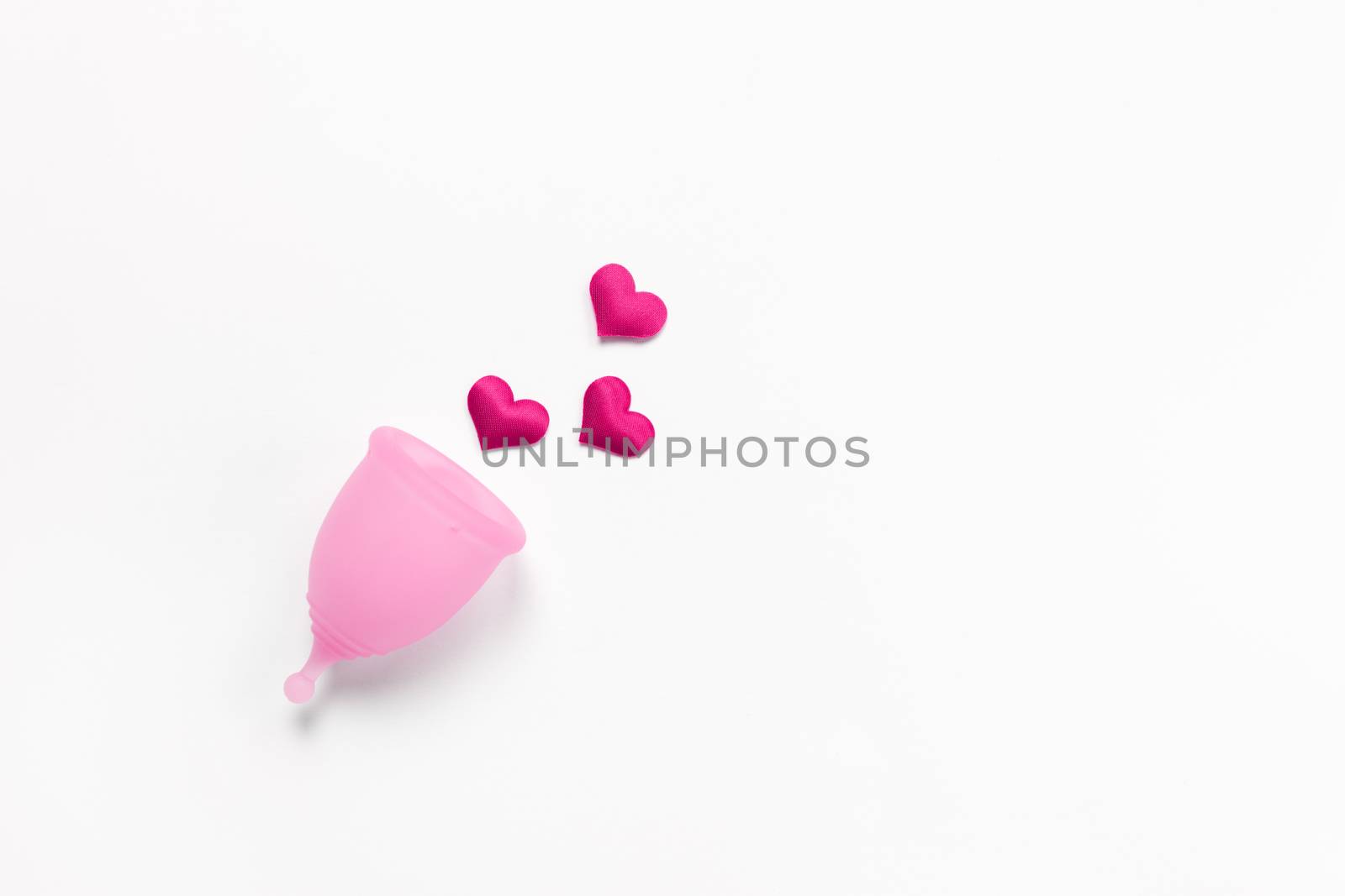 Pink menstrual cup on white background with crimson hearts. Concept zero waste, savings, minimalism, these days. Feminine hygiene product, flat lay, copy space. Horizontal.