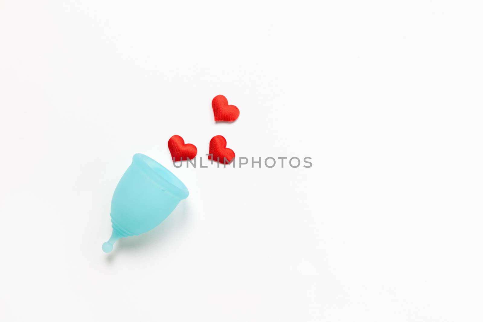 Turquoise menstrual cup on white background with red hearts. Concept zero waste, savings, minimalism, these days. Feminine hygiene product, flat lay, copy space. Horizontal.