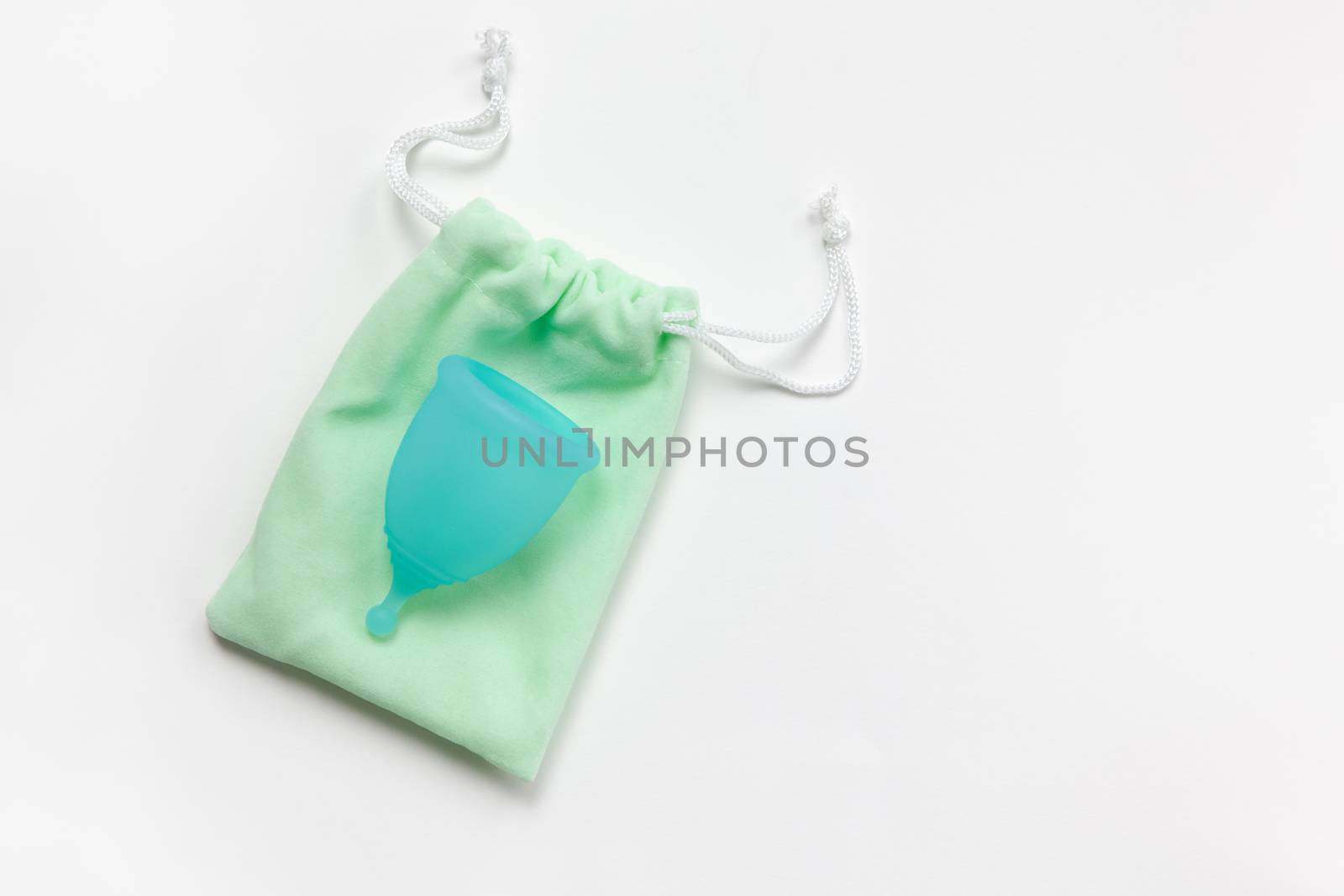 Turquoise menstrual cup on green small bag on white background. Concept zero waste, savings, minimalism, these days. Feminine hygiene product, flat lay, copy space. Horizontal.