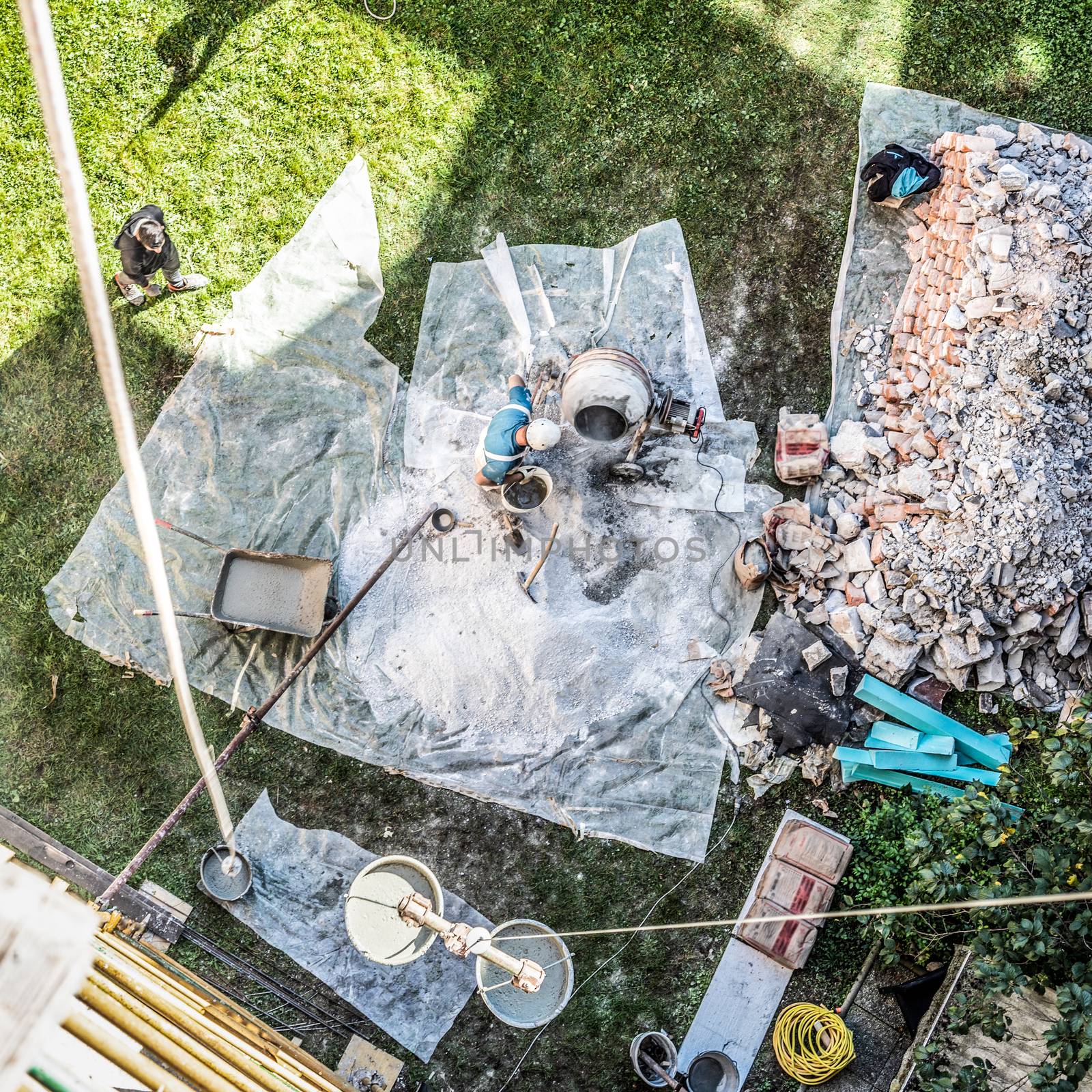 Top view of authentic builder men working with shovel during concrete cement solution mortar preparation in mixer at construction site by kasto