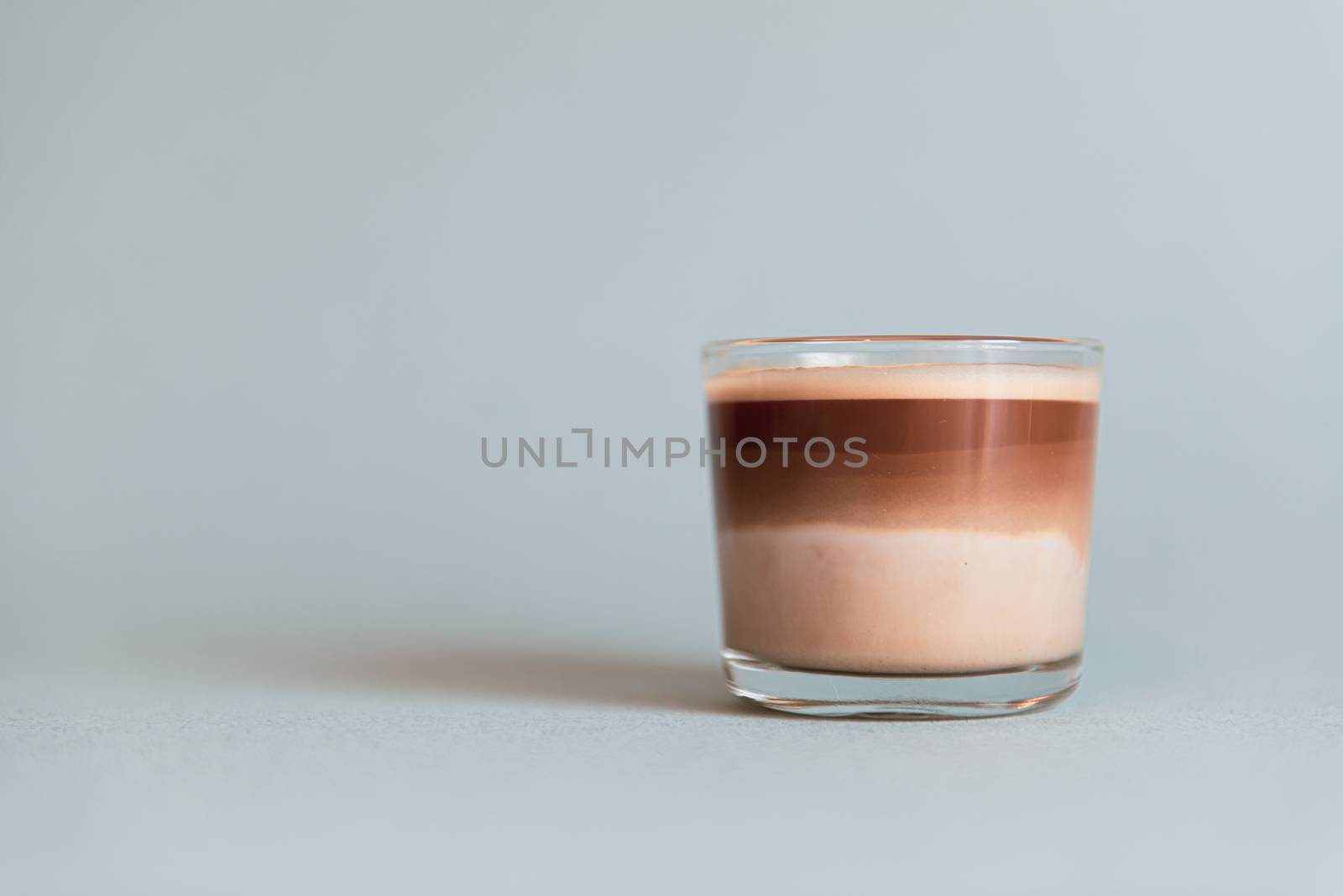 Mini cup of multilayer coffee in a glass cup on grey background.