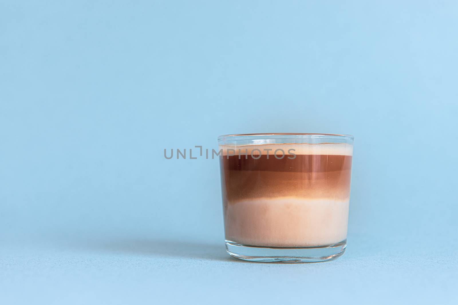 Mini cup of multilayer coffee in a glass cup on blue background.