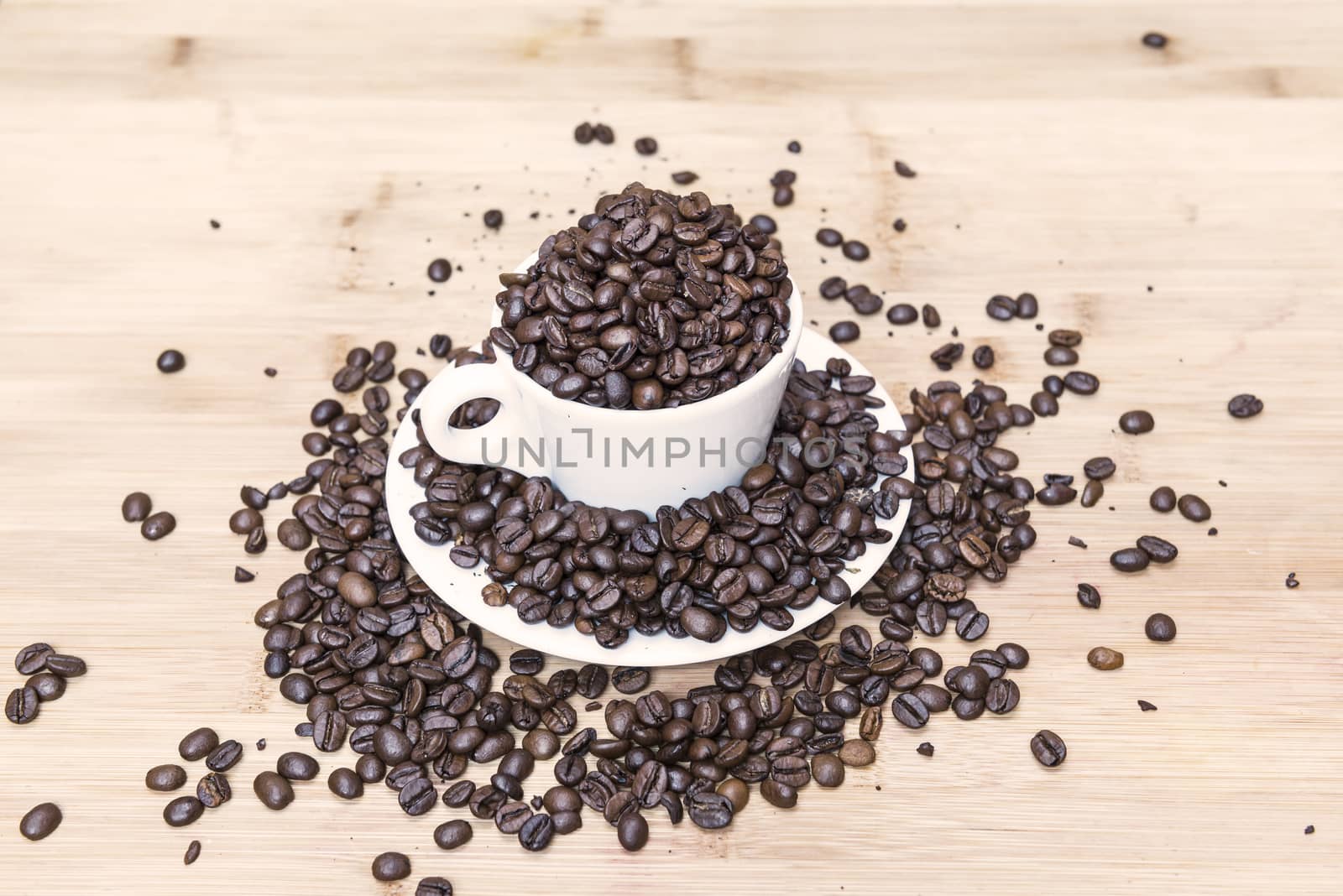 Many coffee beans on wooden background and white cup
