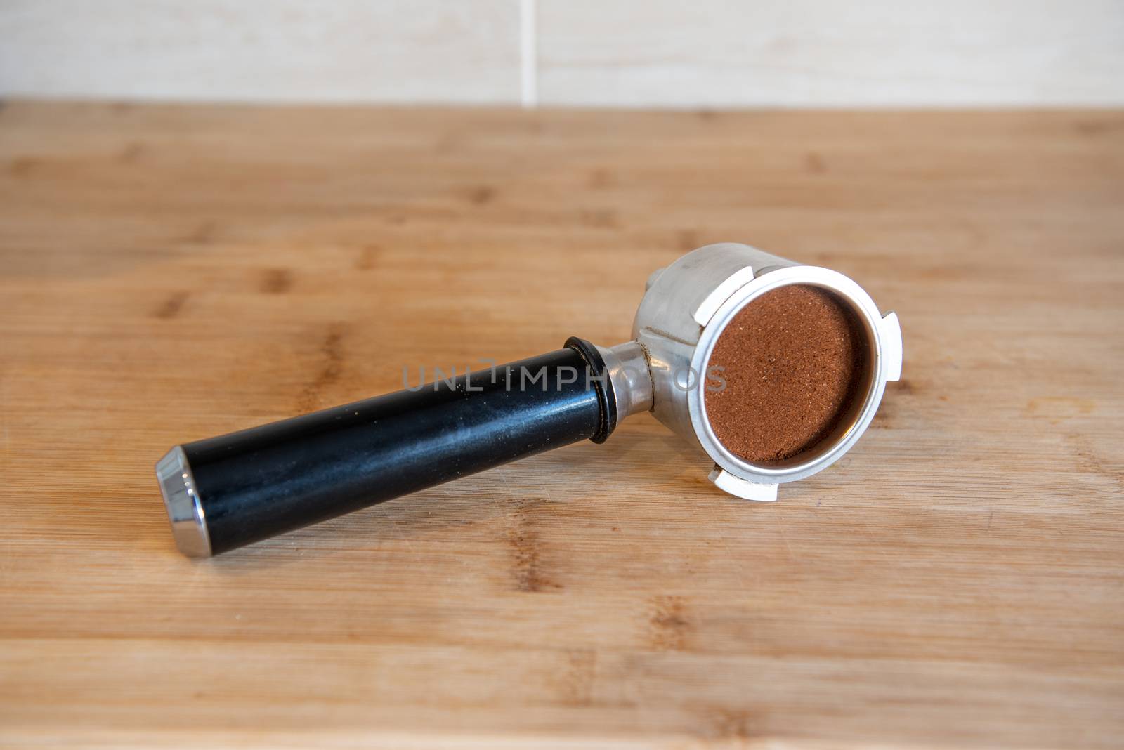 portafilter with temping ground coffee on wooden table.