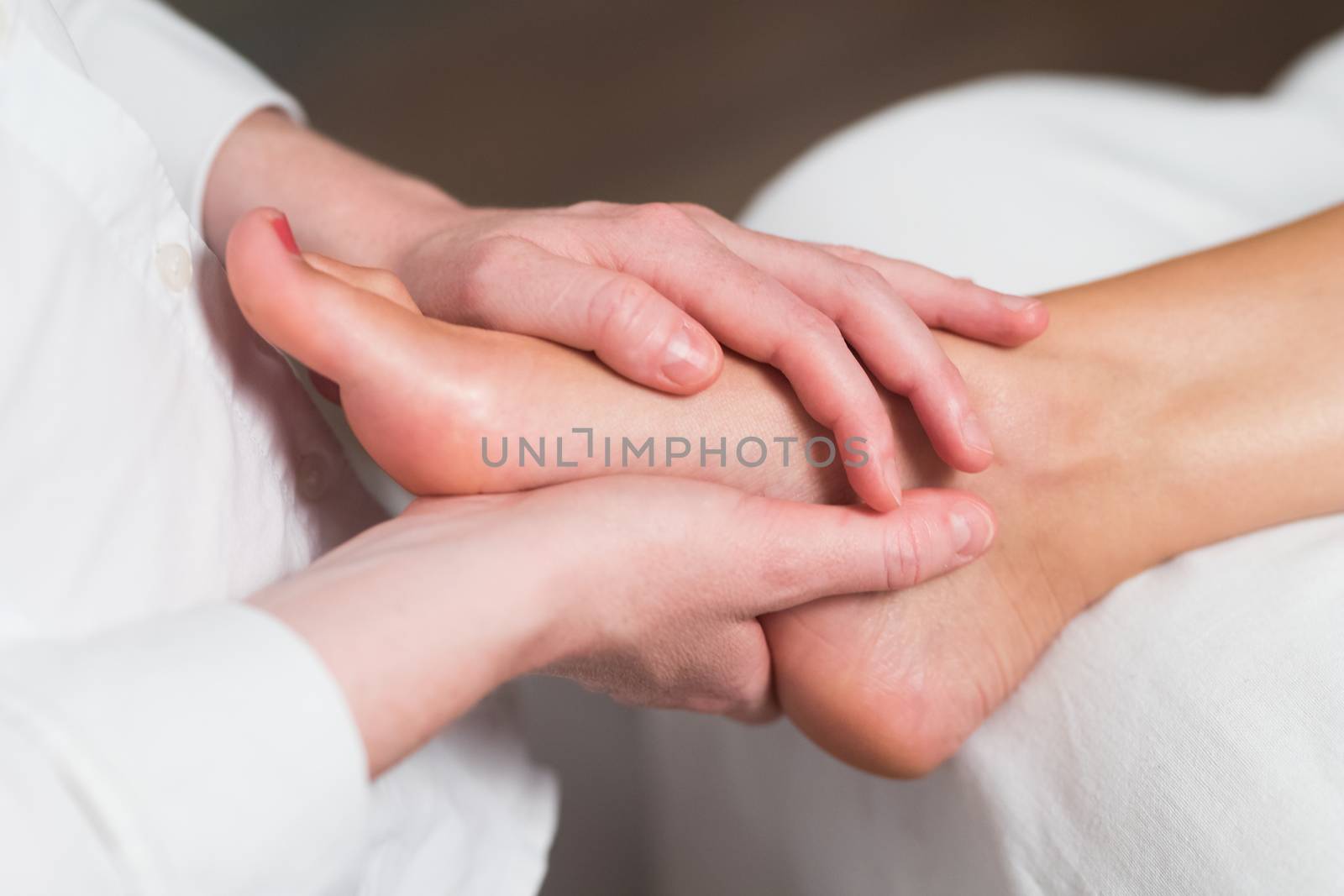Professional female masseur giving reflexology massage to woman foot.