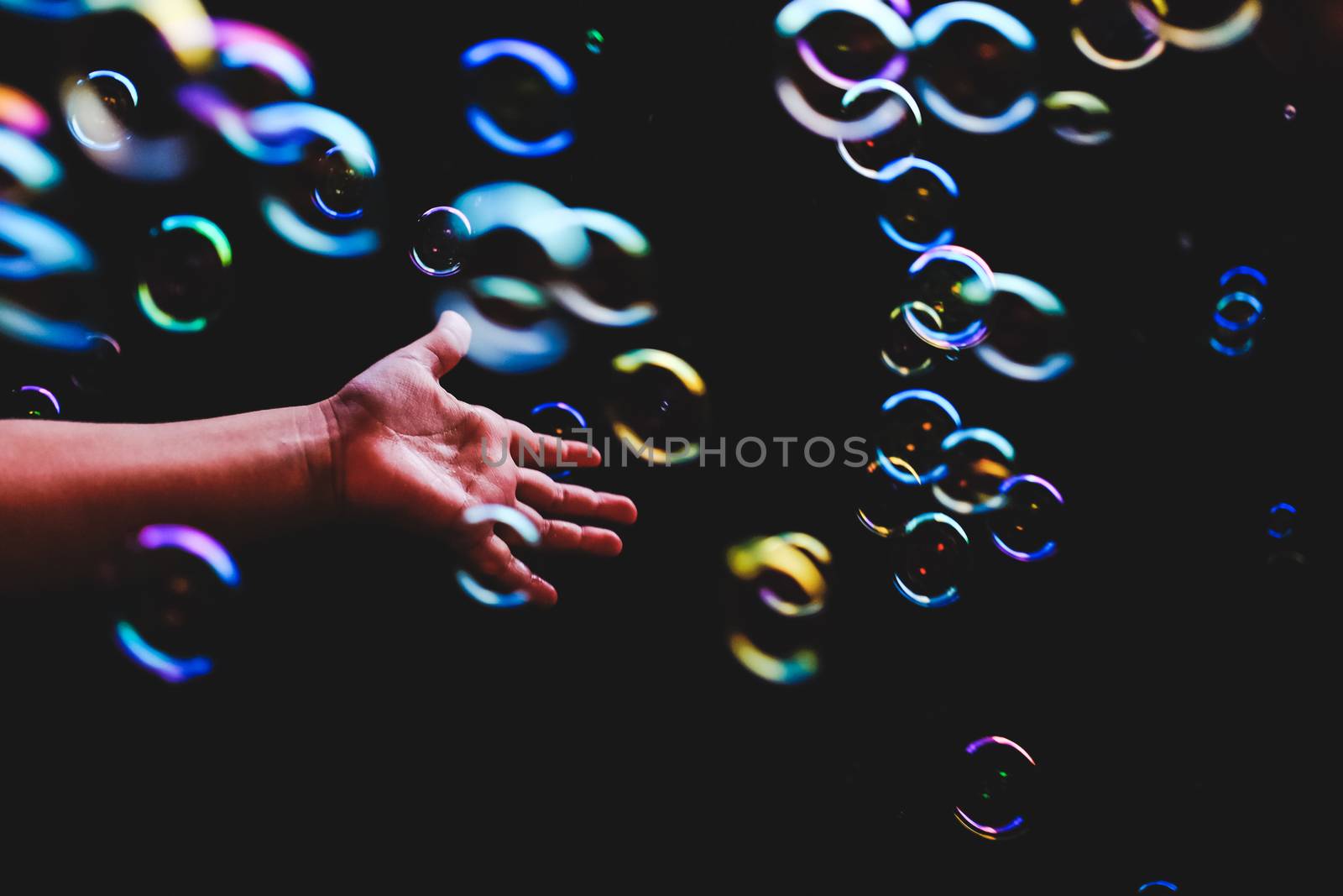 Hand trying to catch colorful bubbles over dark background by mikelju