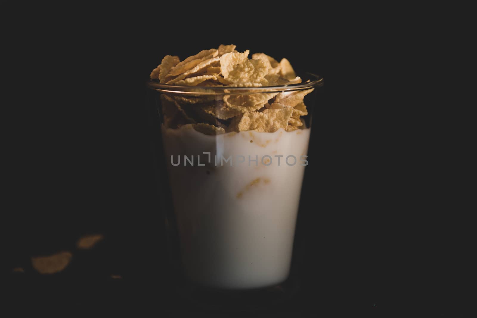 Corn flakes with milk in glass cup isolated on black by marynkin