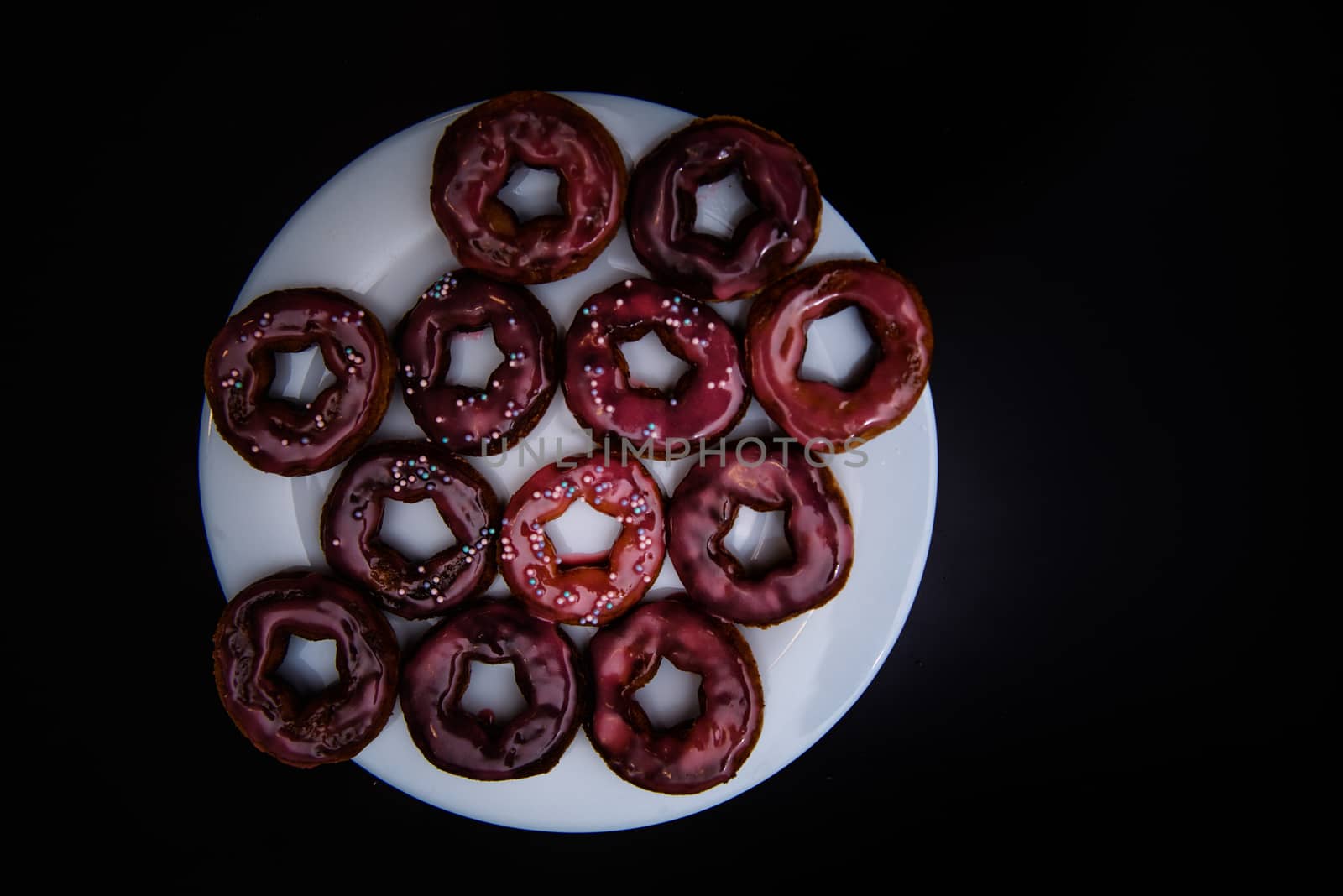 assorted donuts with chocolate frosted, pink glazed and sprinkles donuts. Donuts on white plate with black background