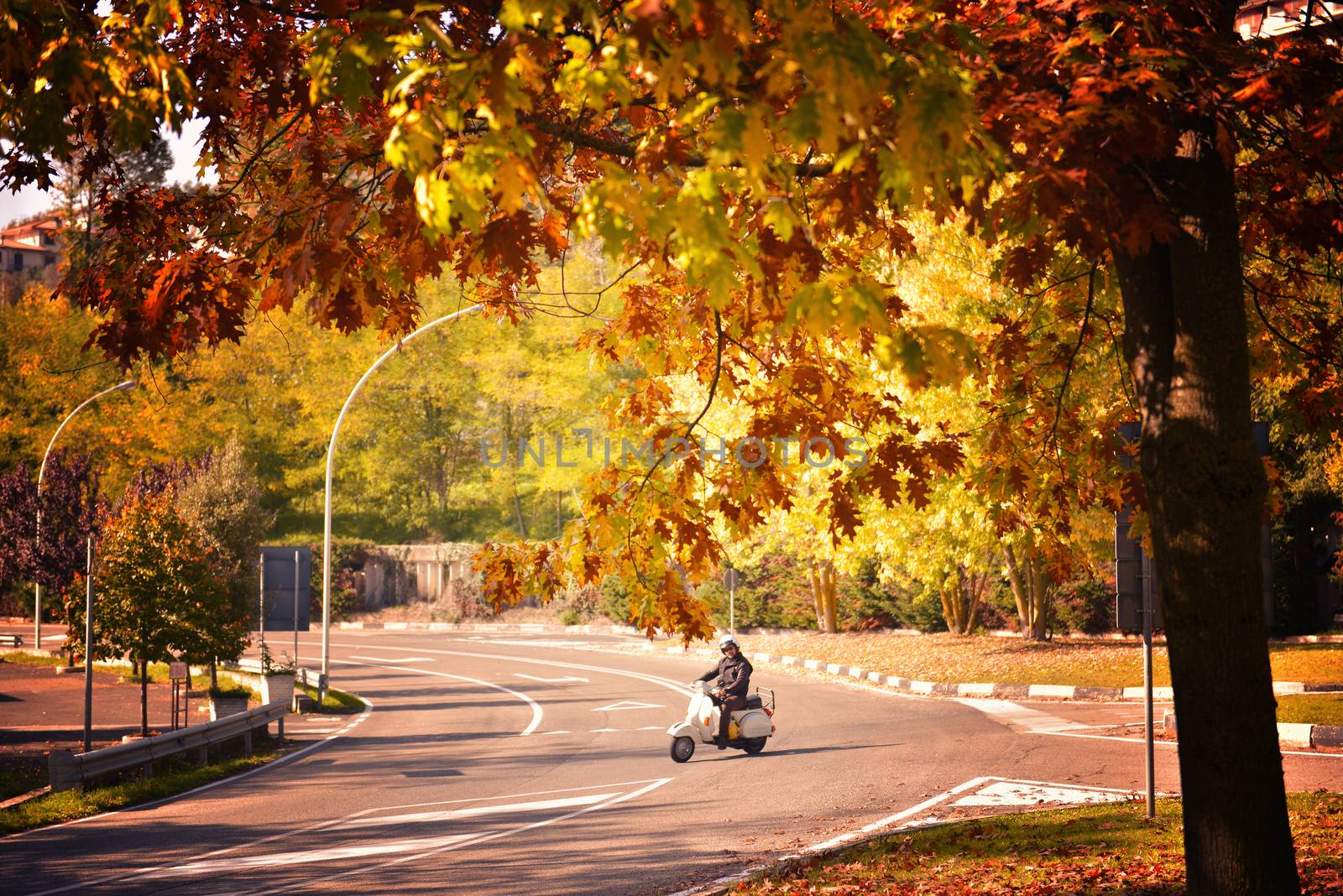 Man riding scooter. Man fun on motorbike ride on his empty way on an autumn, warm day. Transportation and travel for young adult. Tourist exploring town by bike.