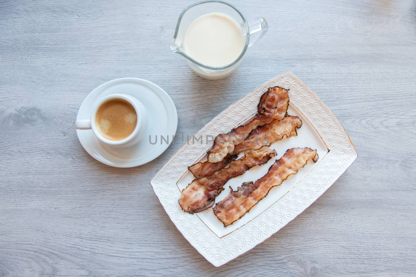 Fried bacon on white plate with cup of coffee and milk jug by marynkin