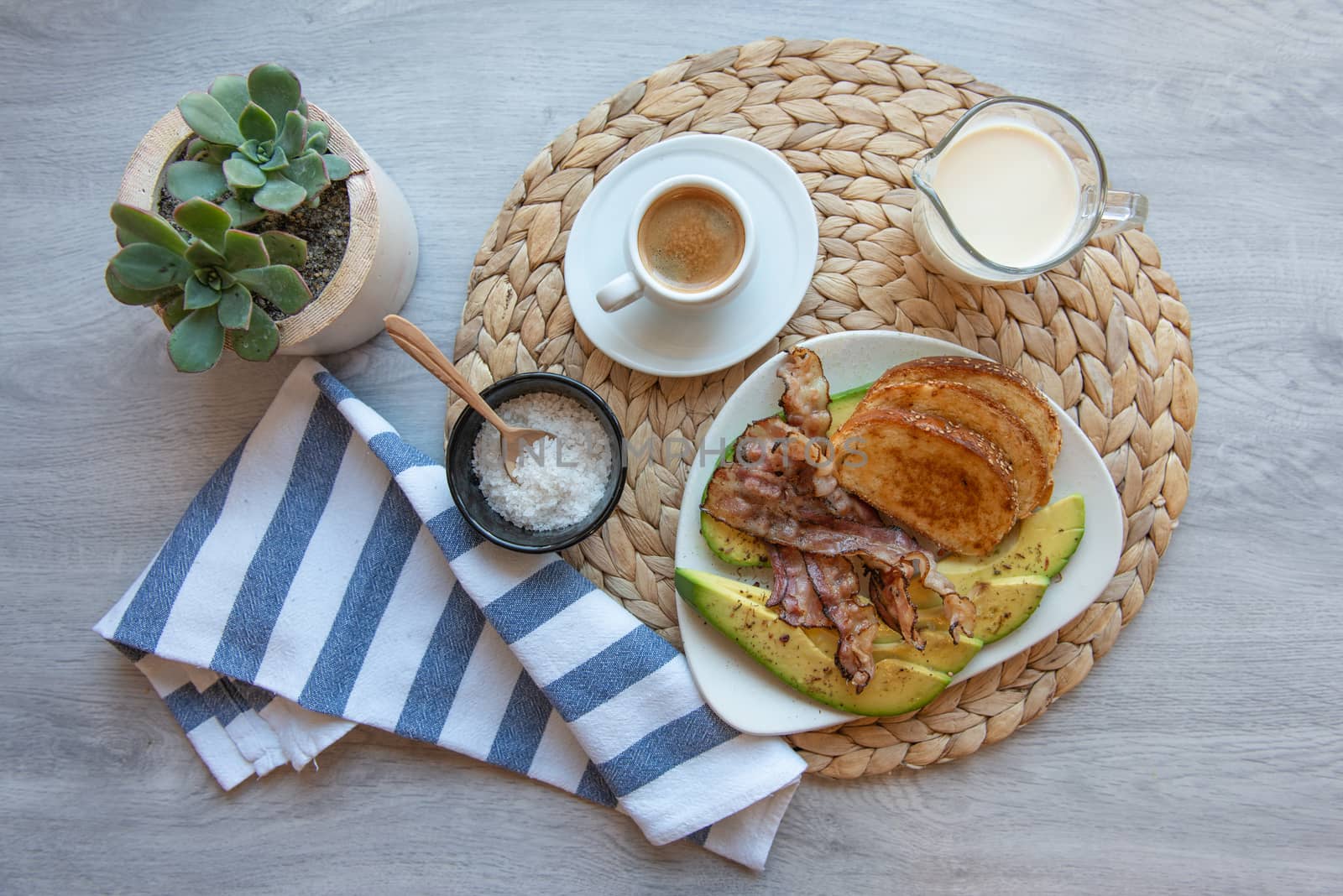 Fried bacon on white plate with cup of coffee, milk jug and toast. Breakfast on gray table