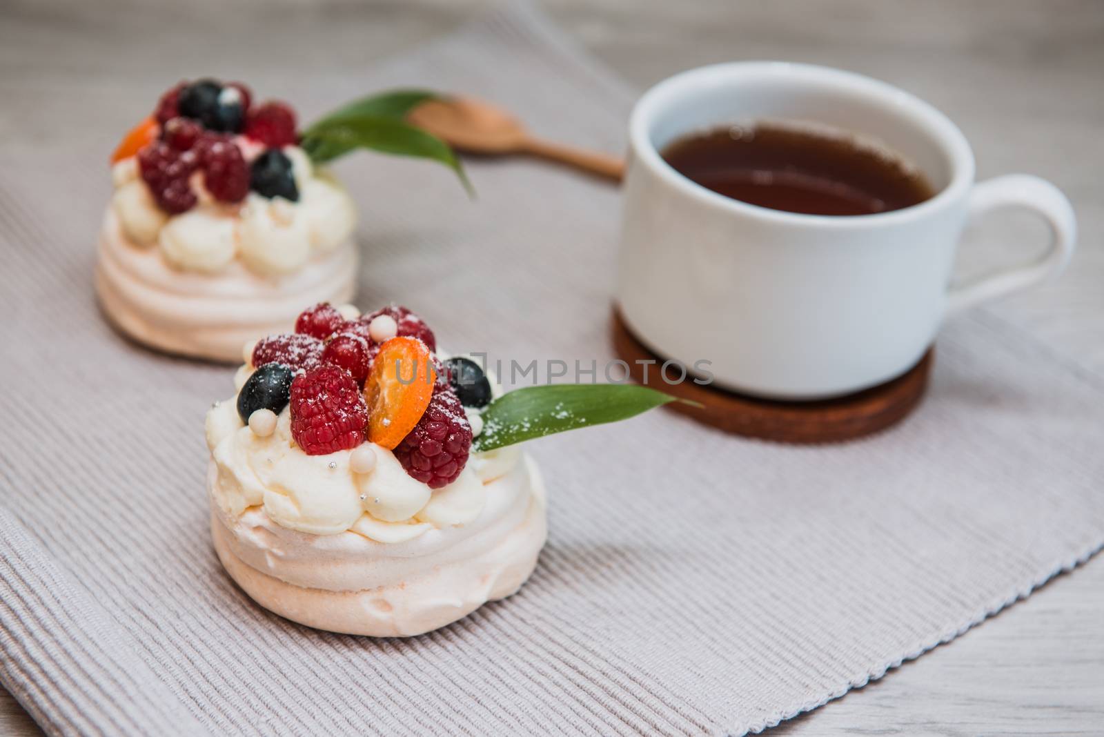 Pavlova meringue desert cake with cream, small fruits and cup of tea