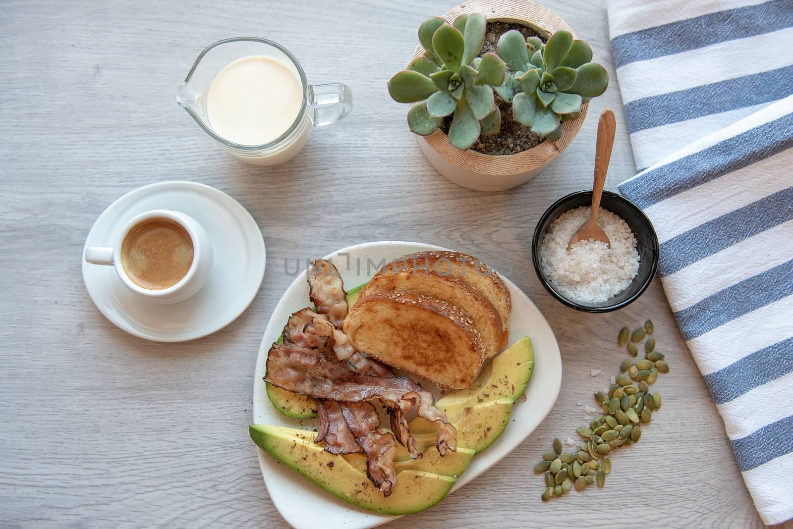 Fried bacon on white plate with cup of coffee, milk jug and toast. Breakfast on gray table