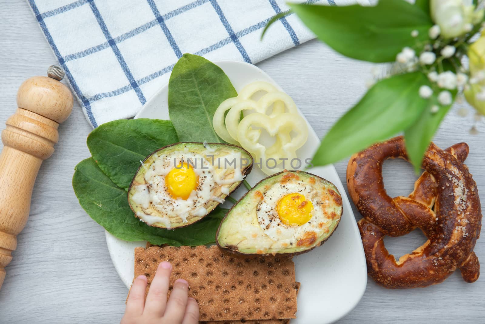 Eggs baked in avocado on plate with with a stretching child's hand by marynkin