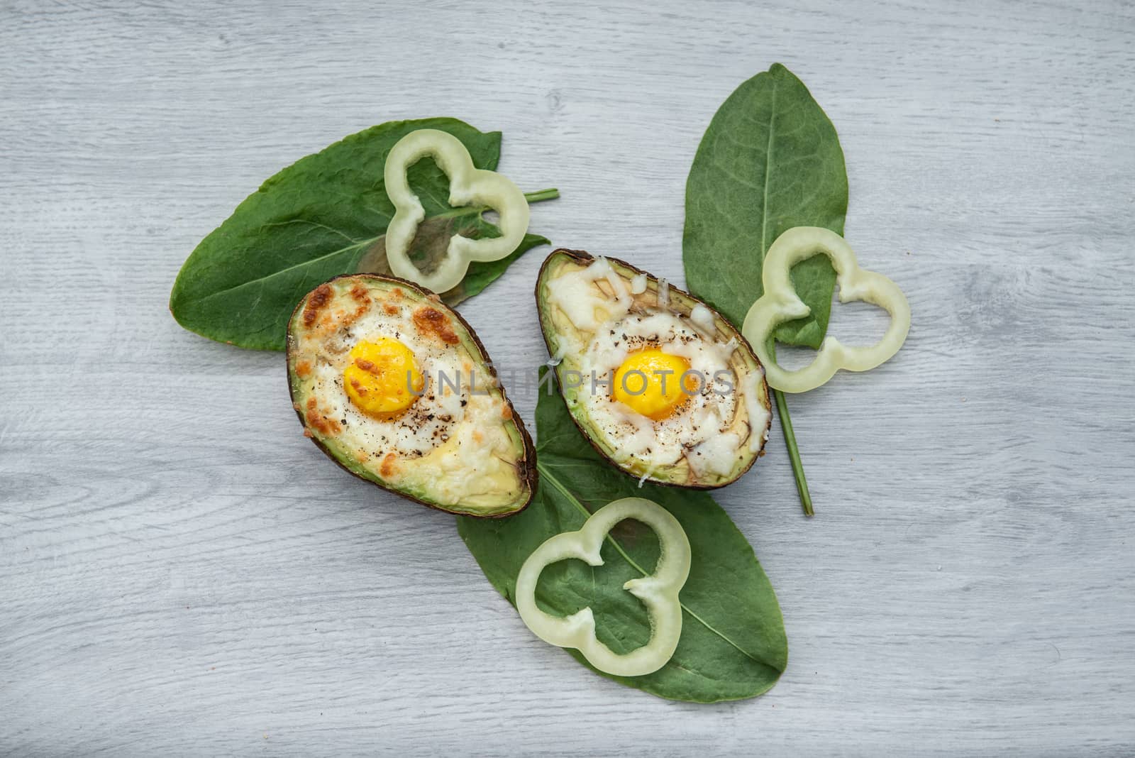 Two Eggs baked in avocado on wooden tabel and green leaves.